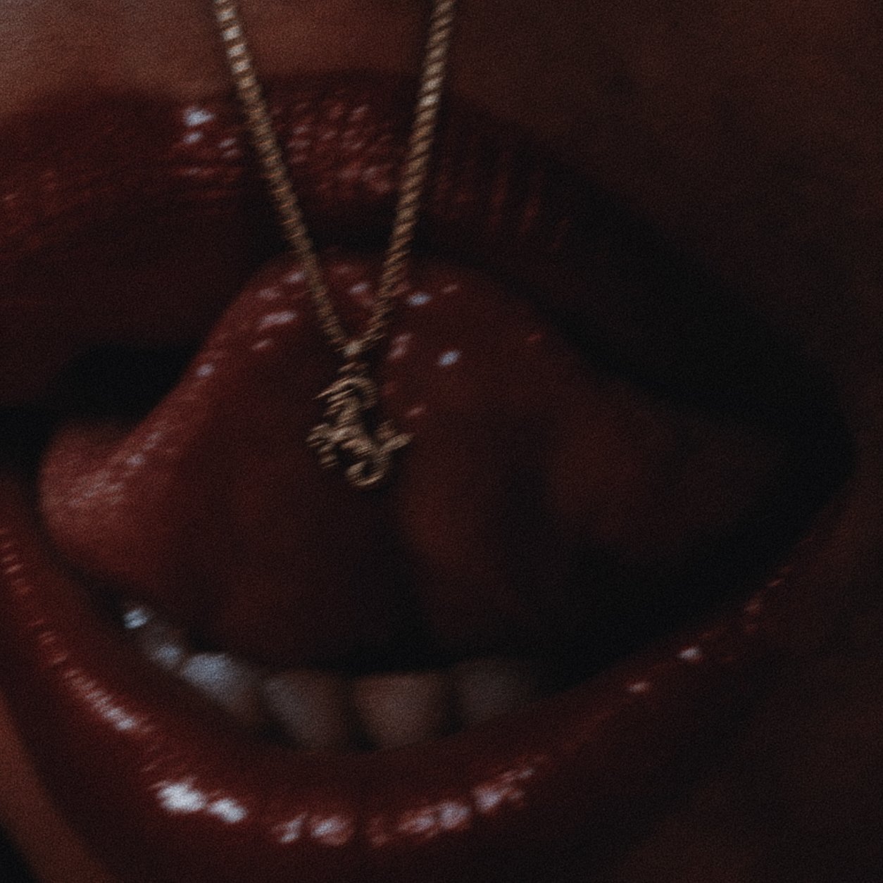 A close-up of a mouth with a gold Capricorn chain necklace.