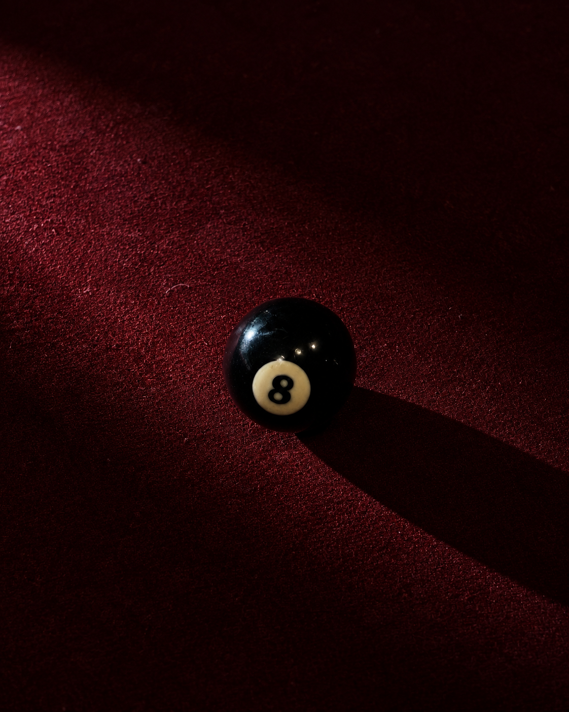 An 8-ball billiard ball on a red textured surface with a shadow cast to the right.