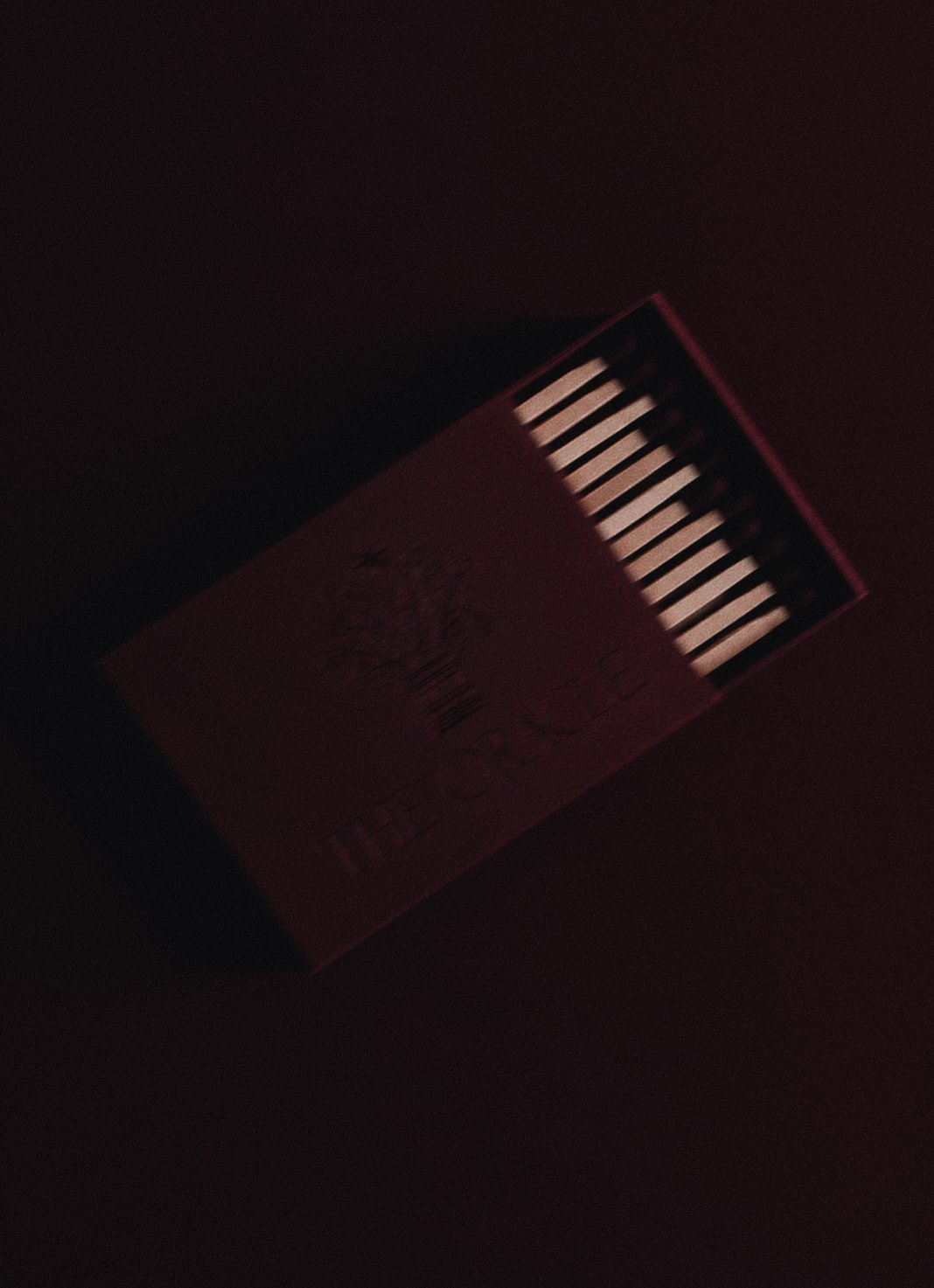 A box of matches with a red and black cover, showing the striking surface and some matchsticks in a dimly lit environment.