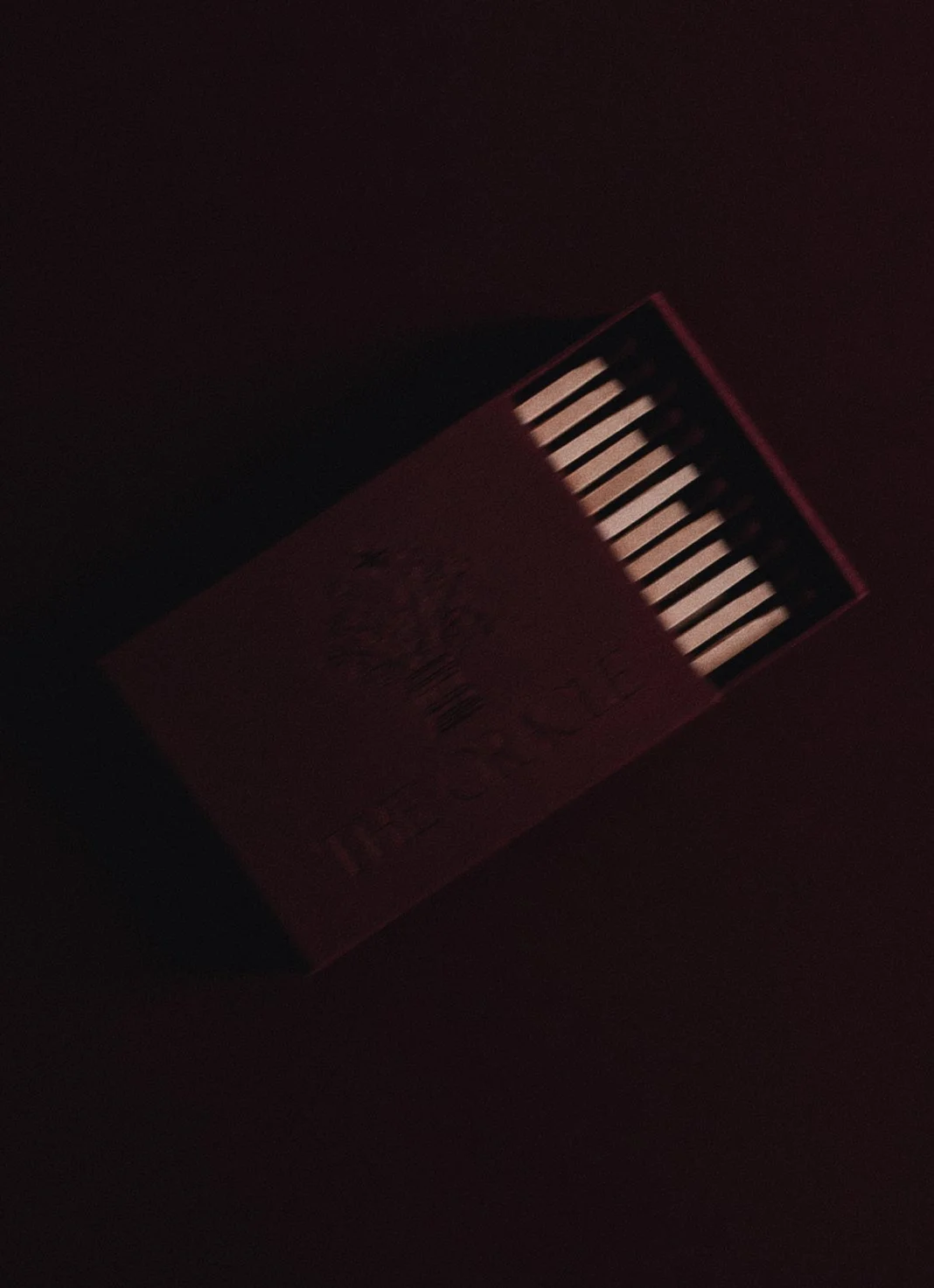 A cigarette pack with lit matches on top, partially illuminated in a dark environment.