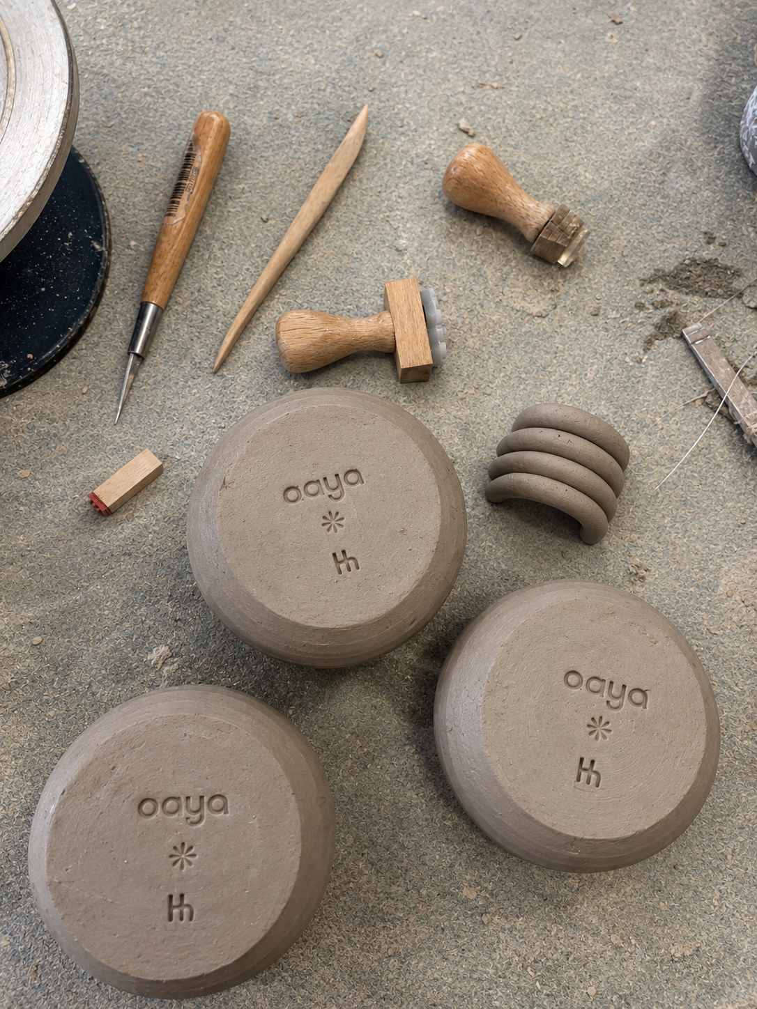 Pots en céramique en cours de fabrication avec outils en bois et en métal, poussière de terre, surface de travail de l'atelier de poterie.