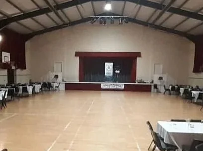Empty community hall with a stage, tables, and chairs, set up for an event.