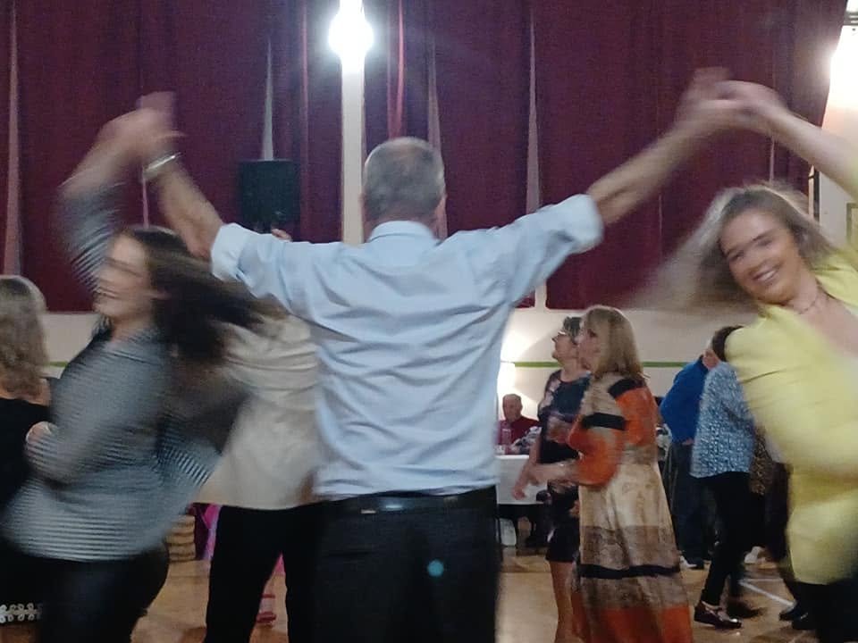 People dancing and having fun at a social gathering or party, with a man spinning women in a circle.