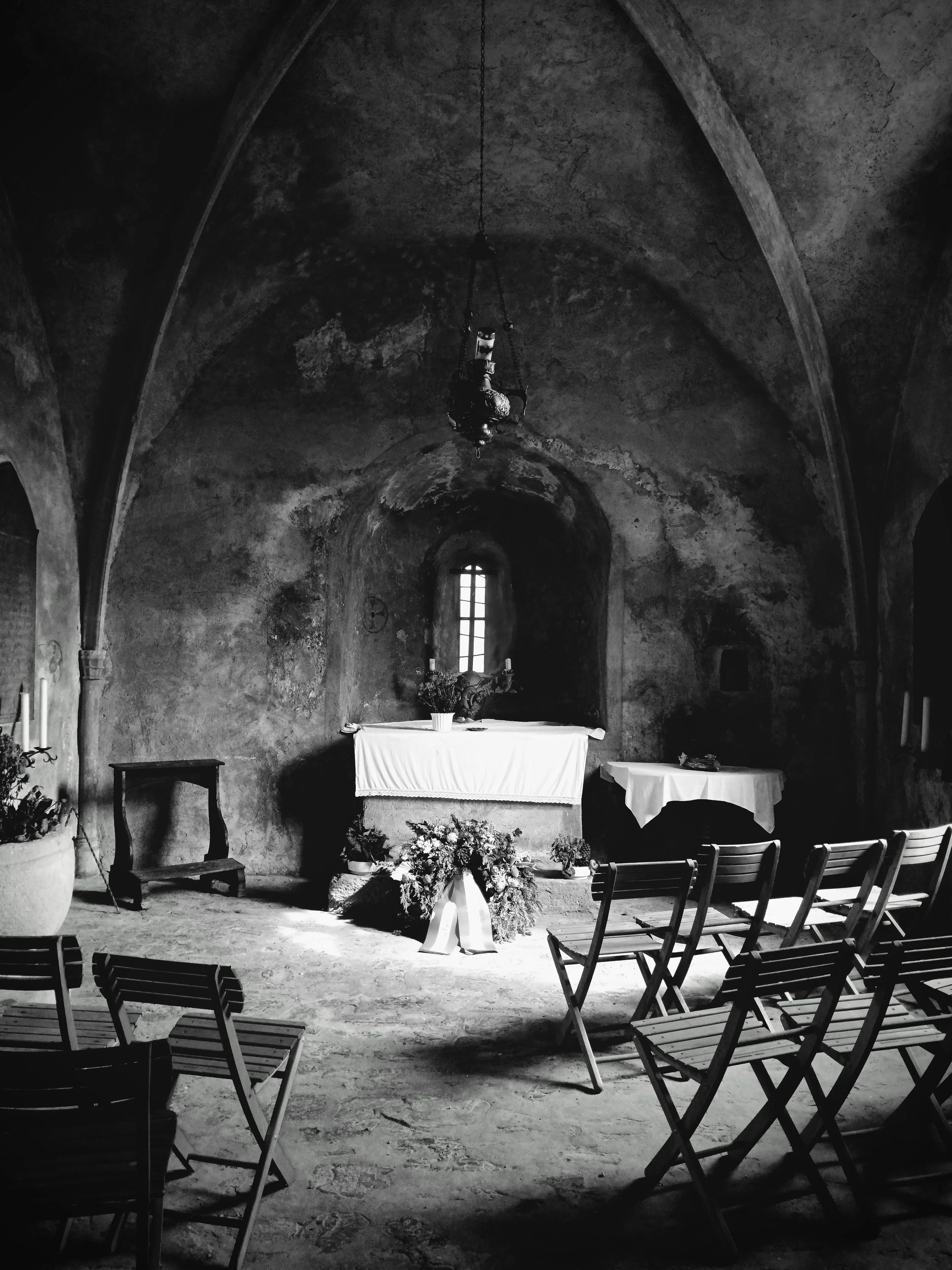 Black and white photo of a rustic, medieval church. There is a small source of light, giving the scene a moody atmosphere.