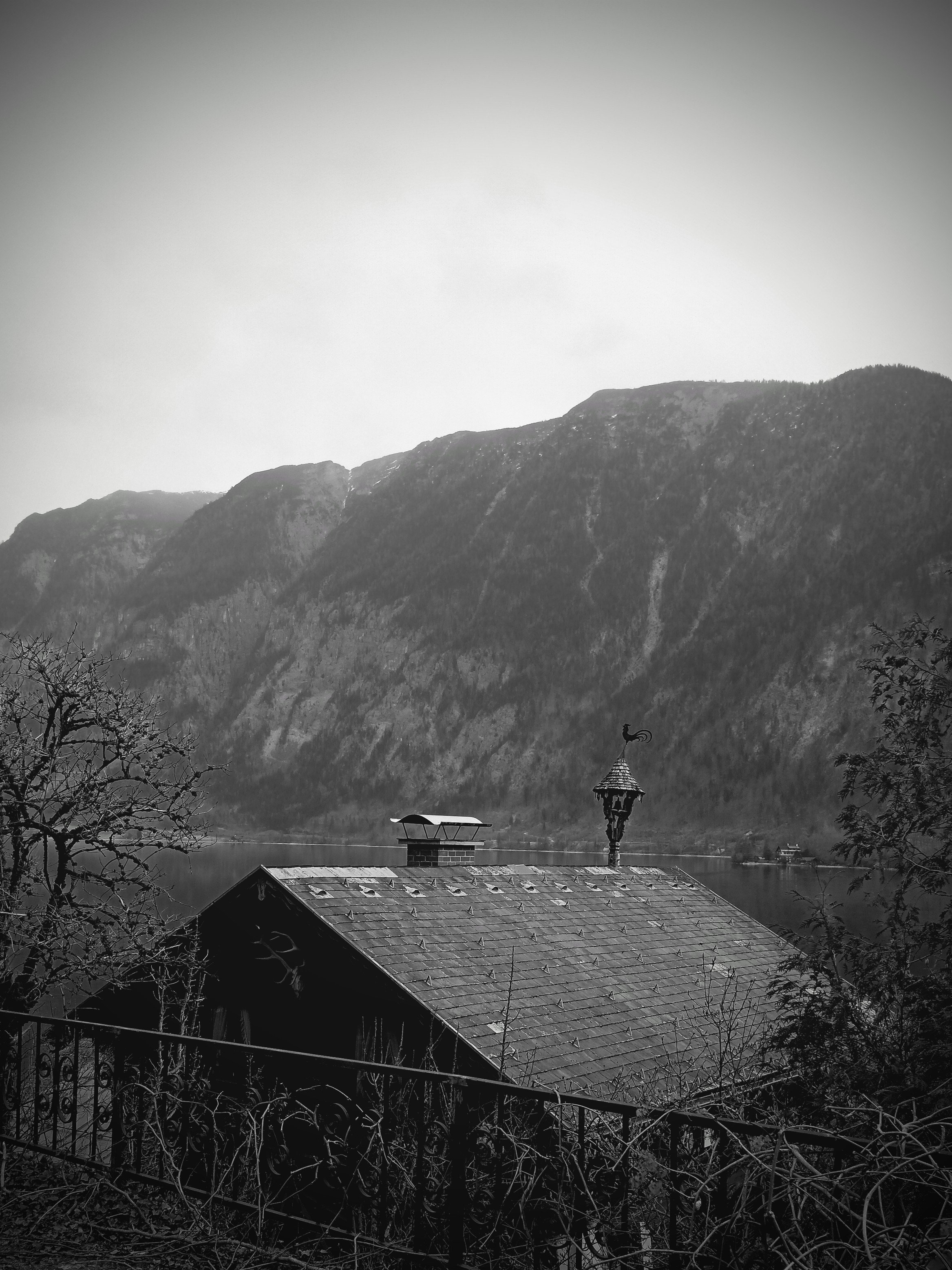 An eerie black and white photo of a mountain range in the background, with a house roof in the foreground. The atmosphere is melancholic.