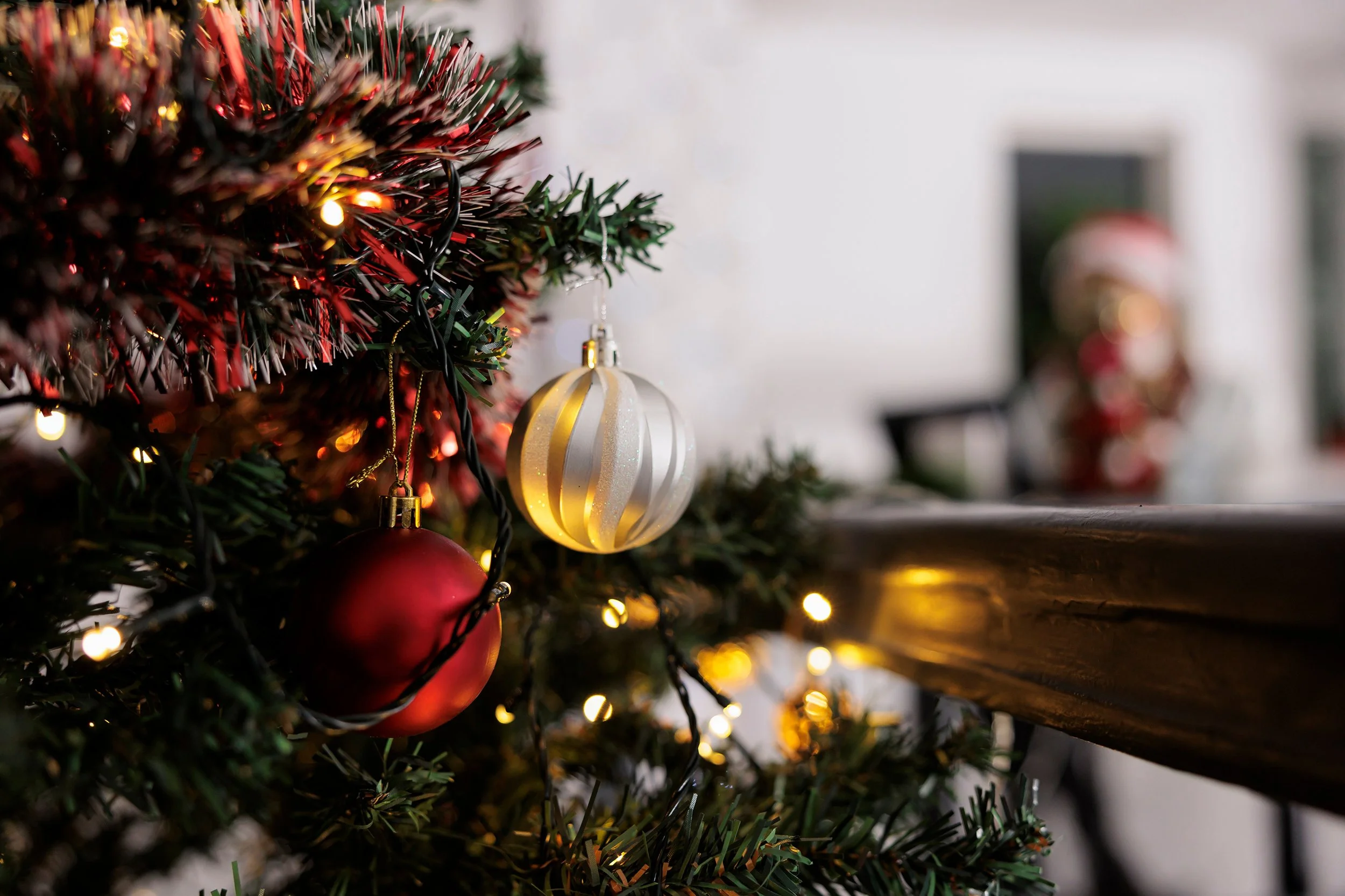 Close-up of a Christmas tree decorated with red and white ornaments and glowing string lights beside a fireplace.