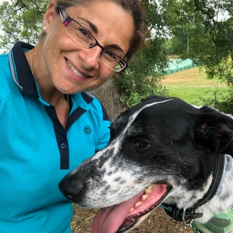 Smiling woman wearing glasses takes a selfie with a black-and-white dog outdoors.