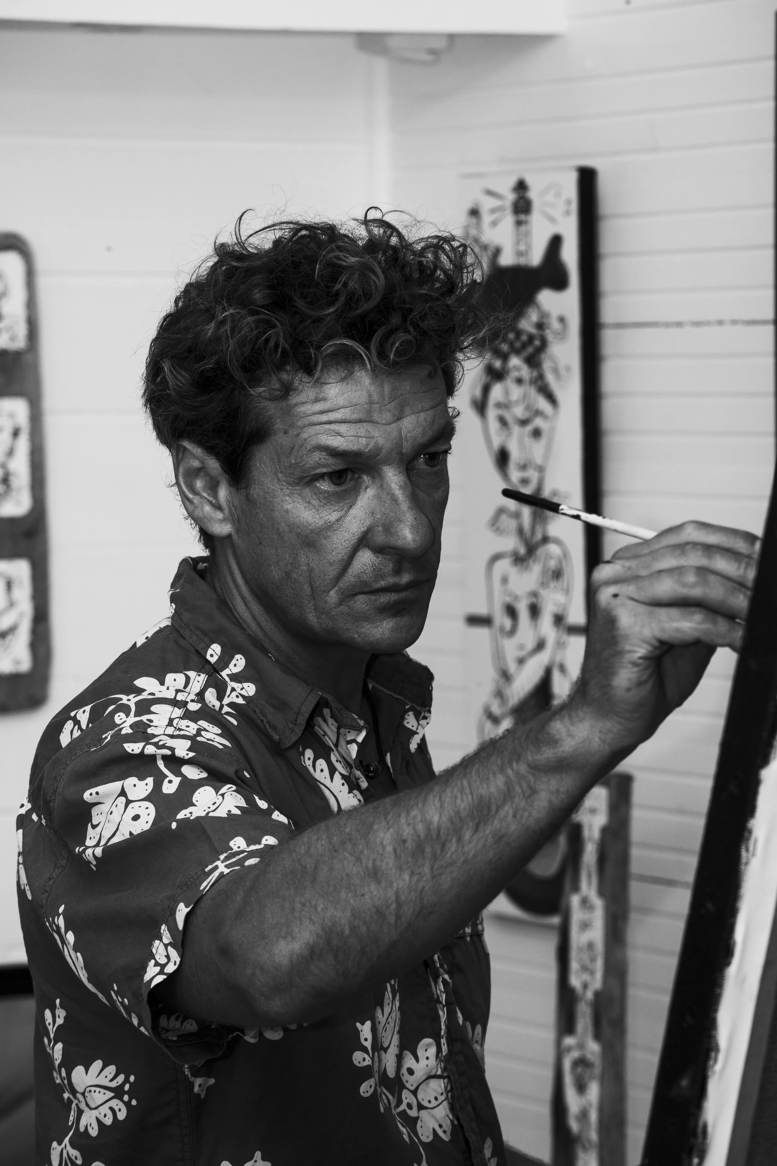 Un homme avec des cheveux bouclés peignant une œuvre d'art dans un atelier.