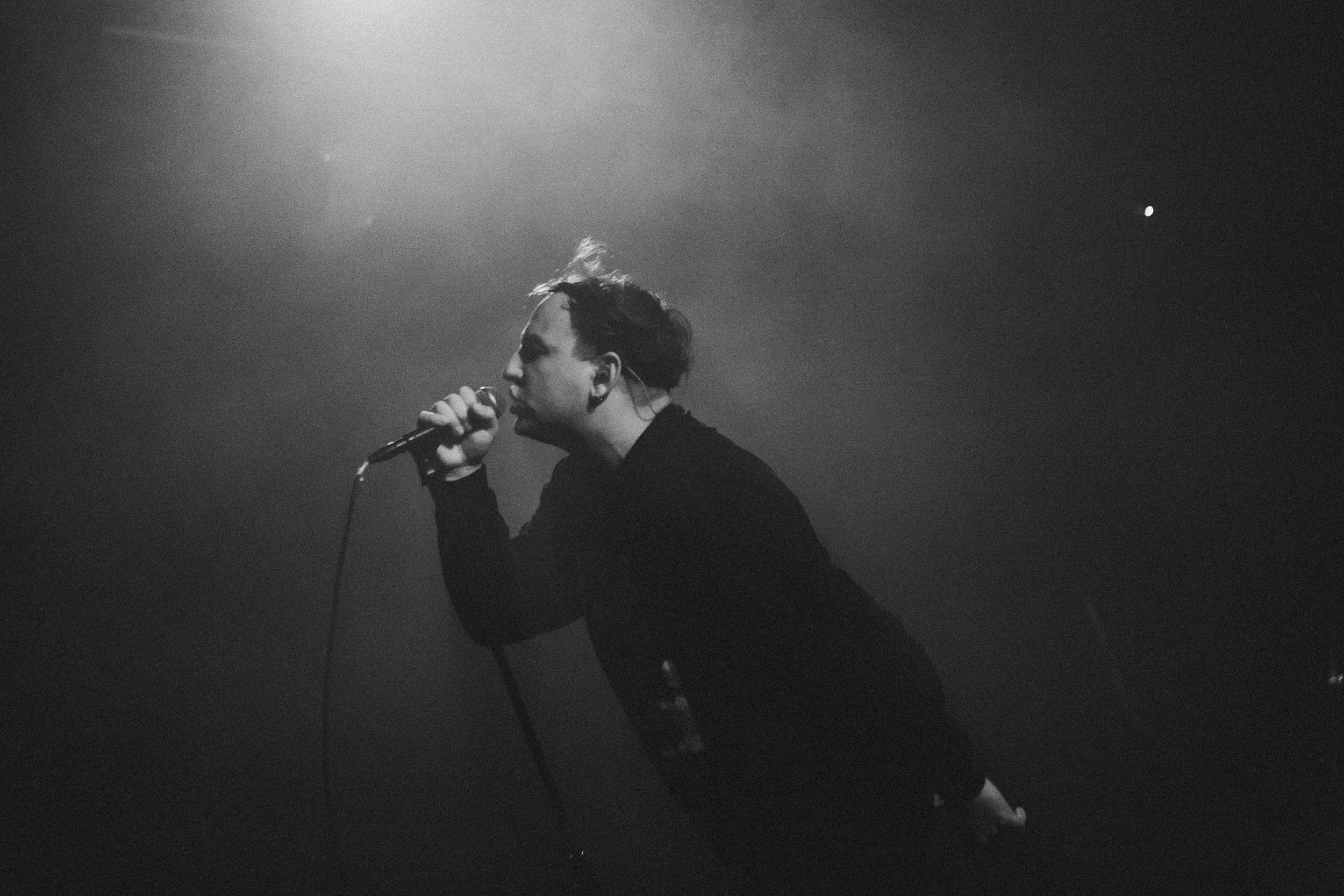 Une personne chante en tenant un microphone dans une ambiance sombre, en noir et blanc, avec la lune visible dans le ciel.