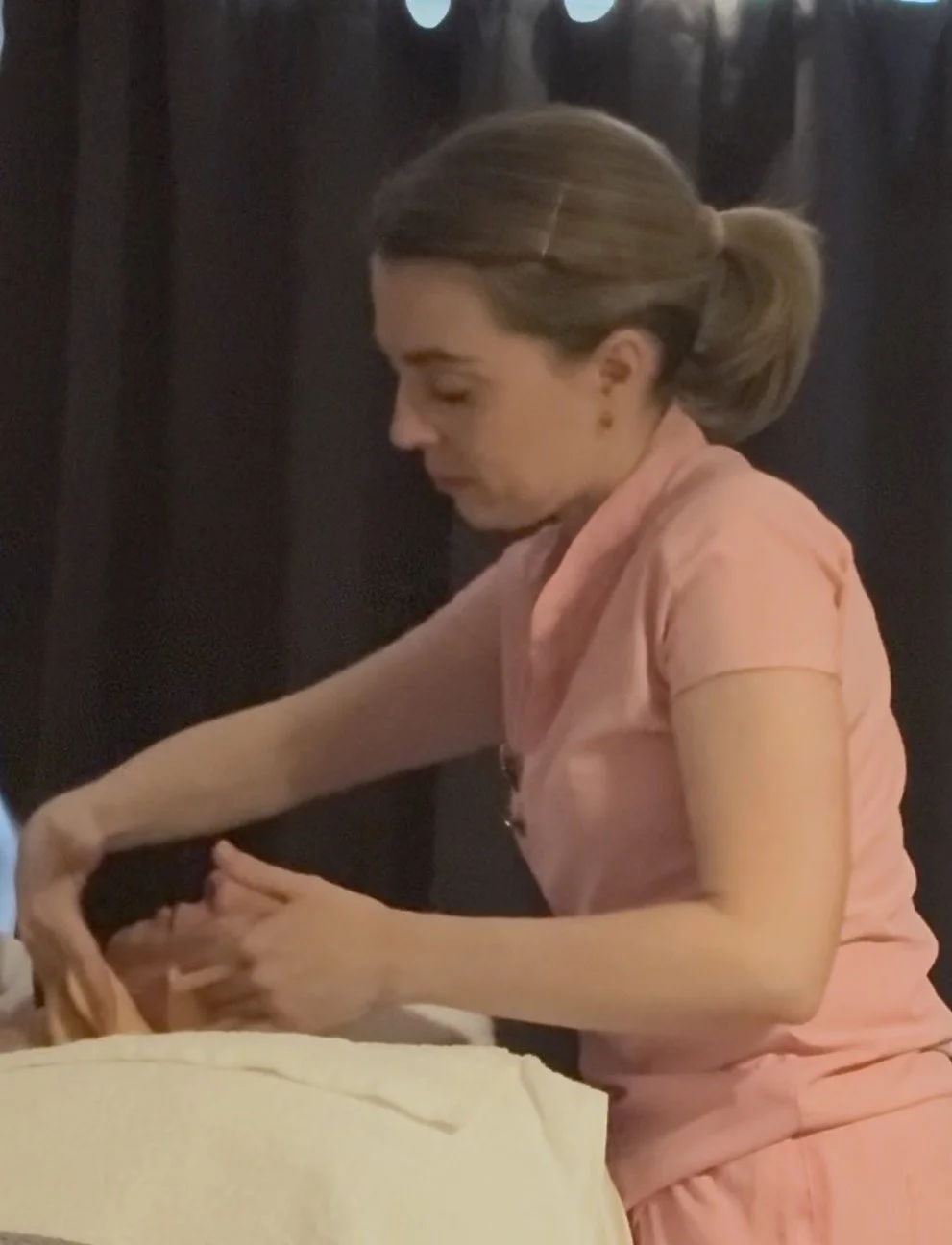 A woman in pink scrubs tending to a pig in a pen.