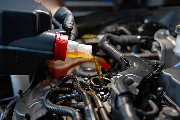 A person pouring engine oil into a car engine with a yellow liquid oil container.