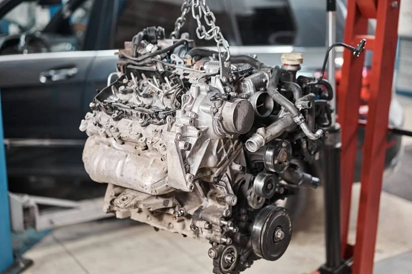 Car engine hanging on a chain hoist in an automotive repair shop.