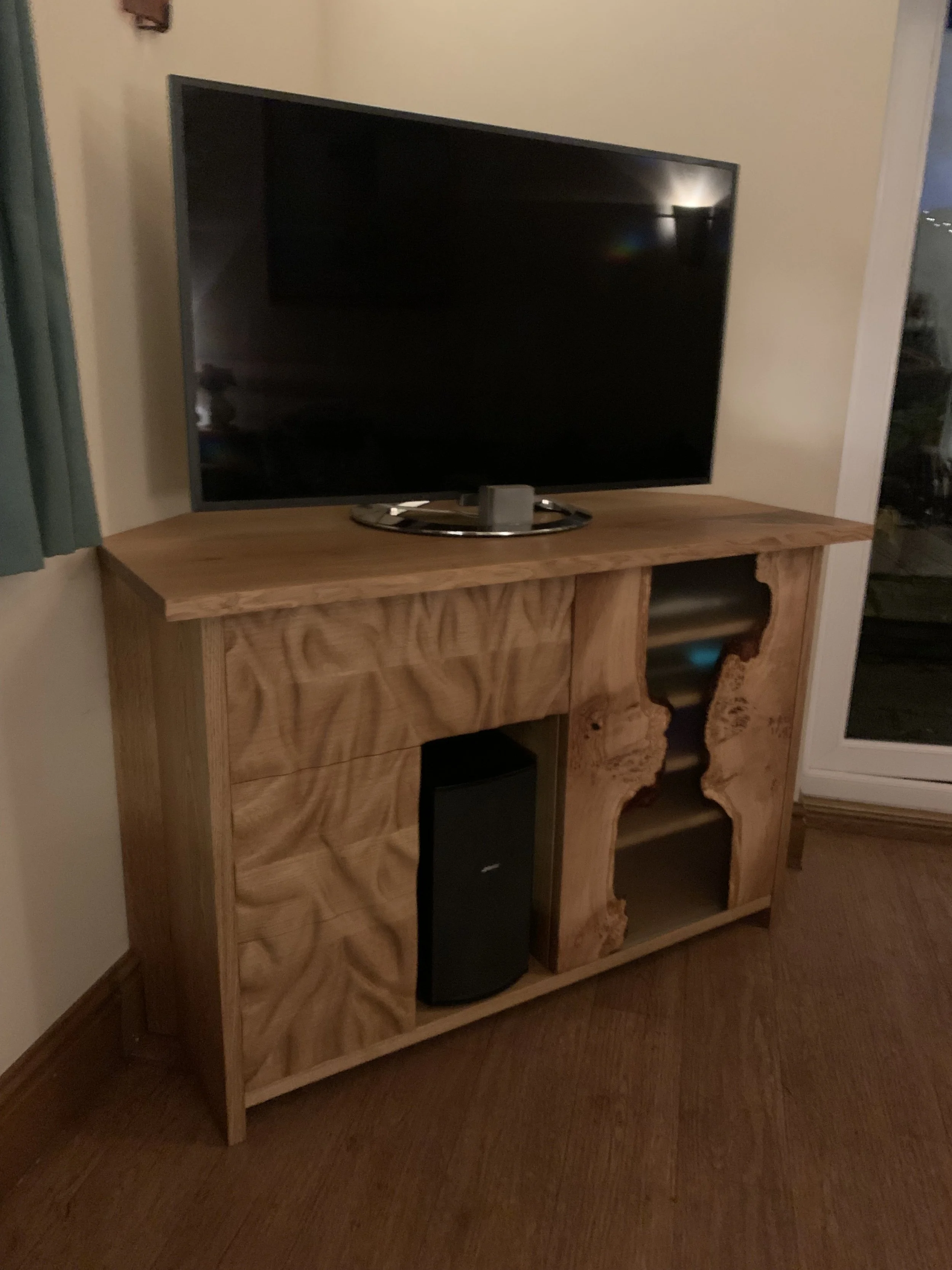 A wooden entertainment center with a flat-screen TV on top and a black speaker inside one of the open shelves, placed on a carpeted floor in a room.
