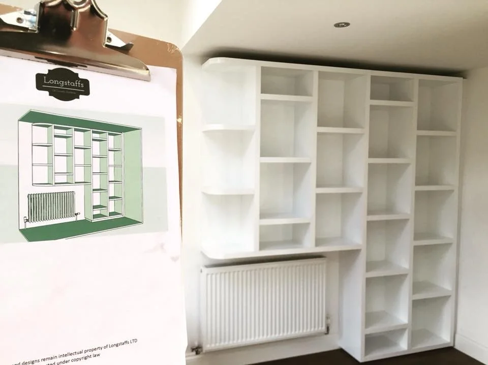 Empty white built-in bookshelf with multiple shelves and a radiator below, in a room with plain white walls and ceiling.