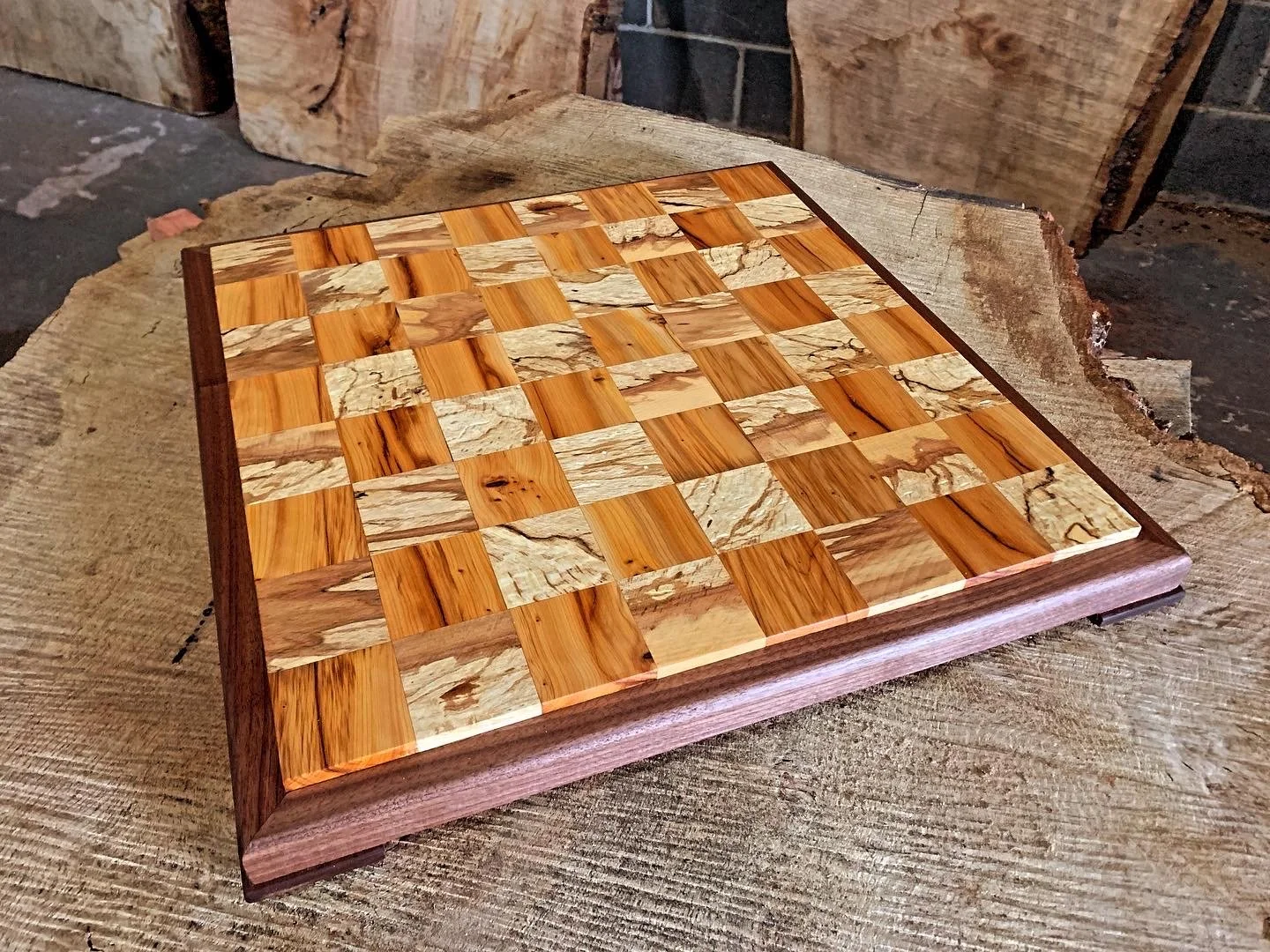 A wooden chessboard with alternating light and dark squares, placed on a rustic wooden surface.