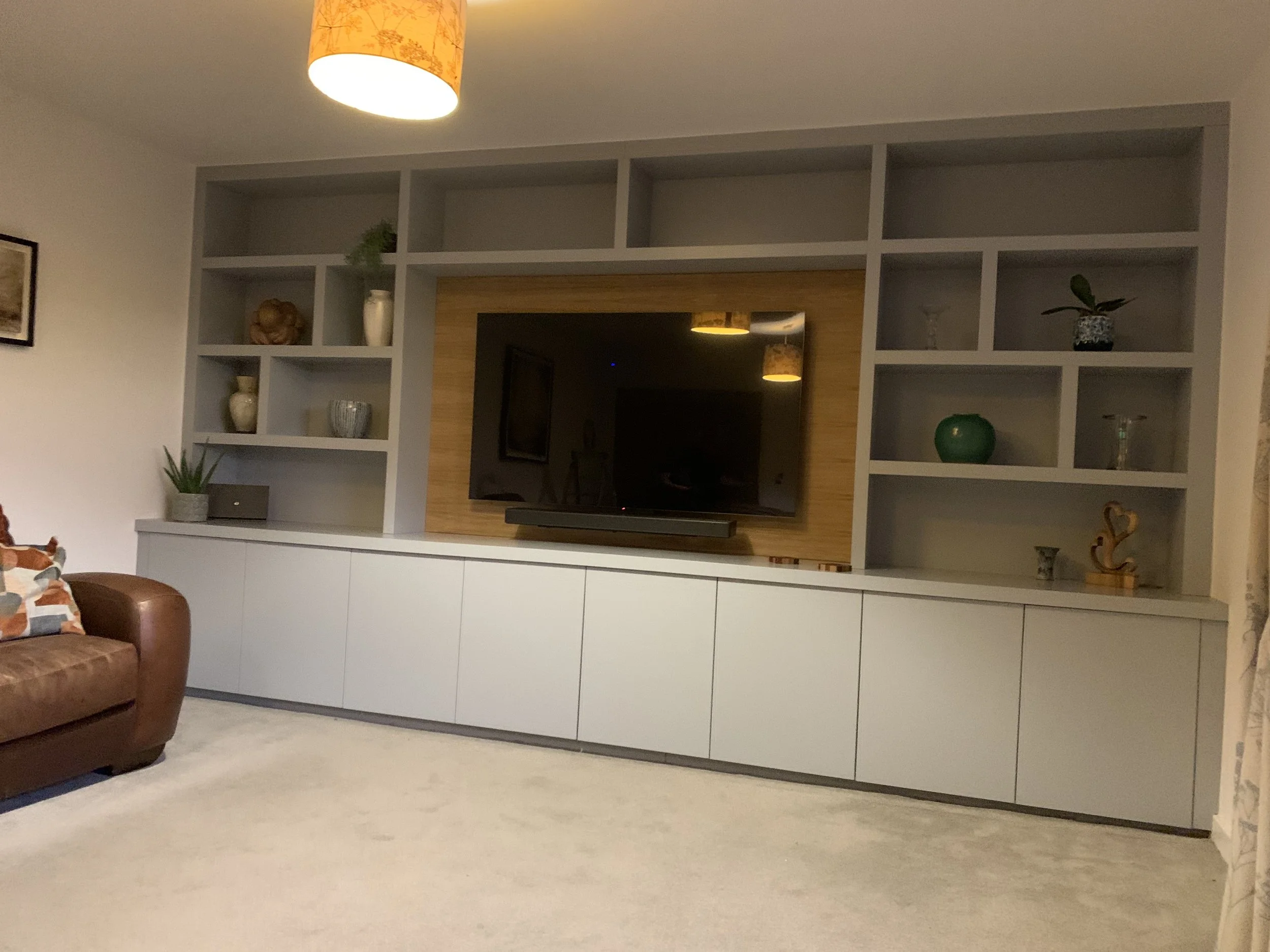 Living room with a built-in shelving unit, a mounted flat-screen TV, and a brown armchair.