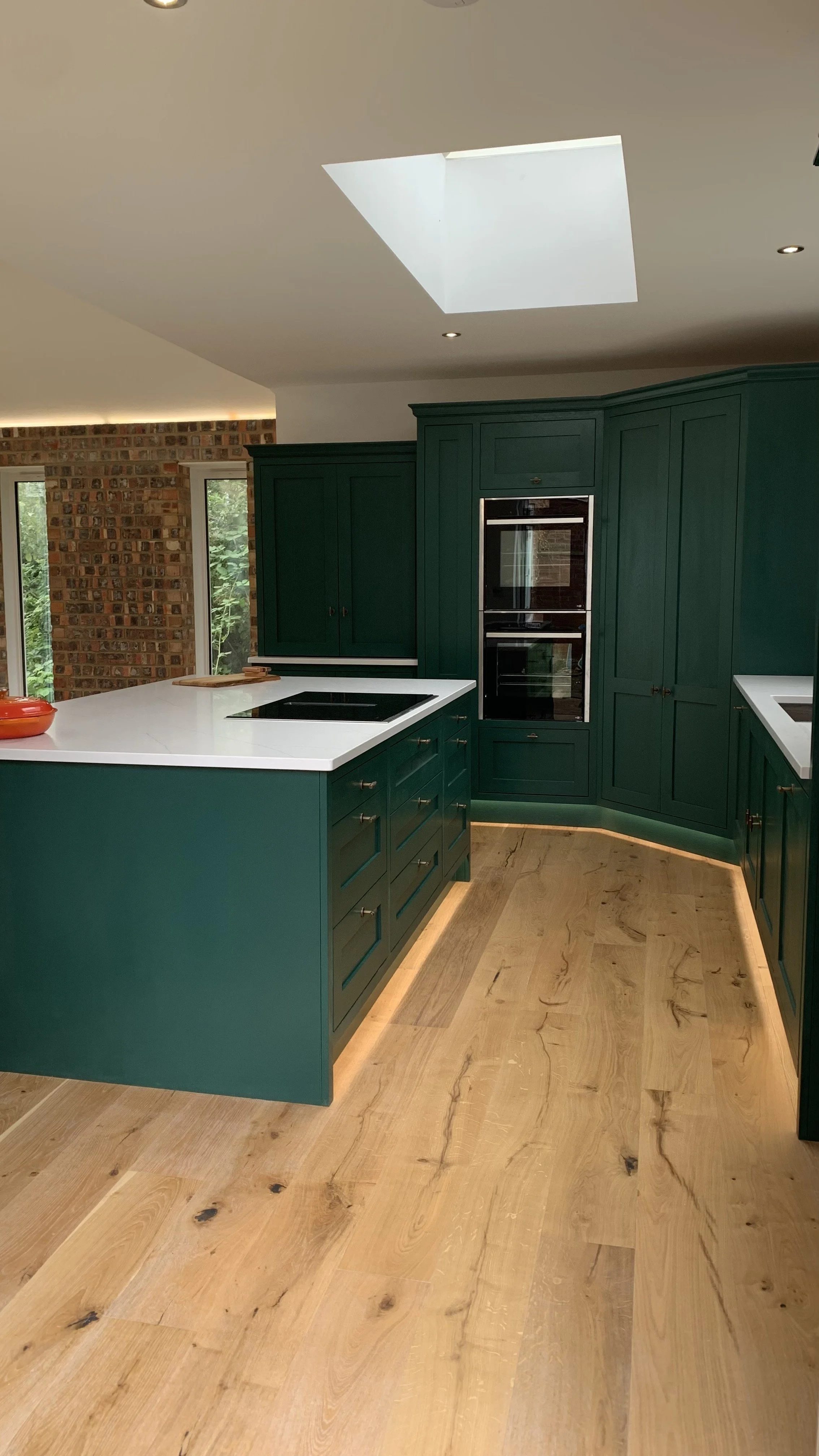 A modern kitchen with teal cabinetry, white countertops, wooden flooring, and a ceiling skylight.