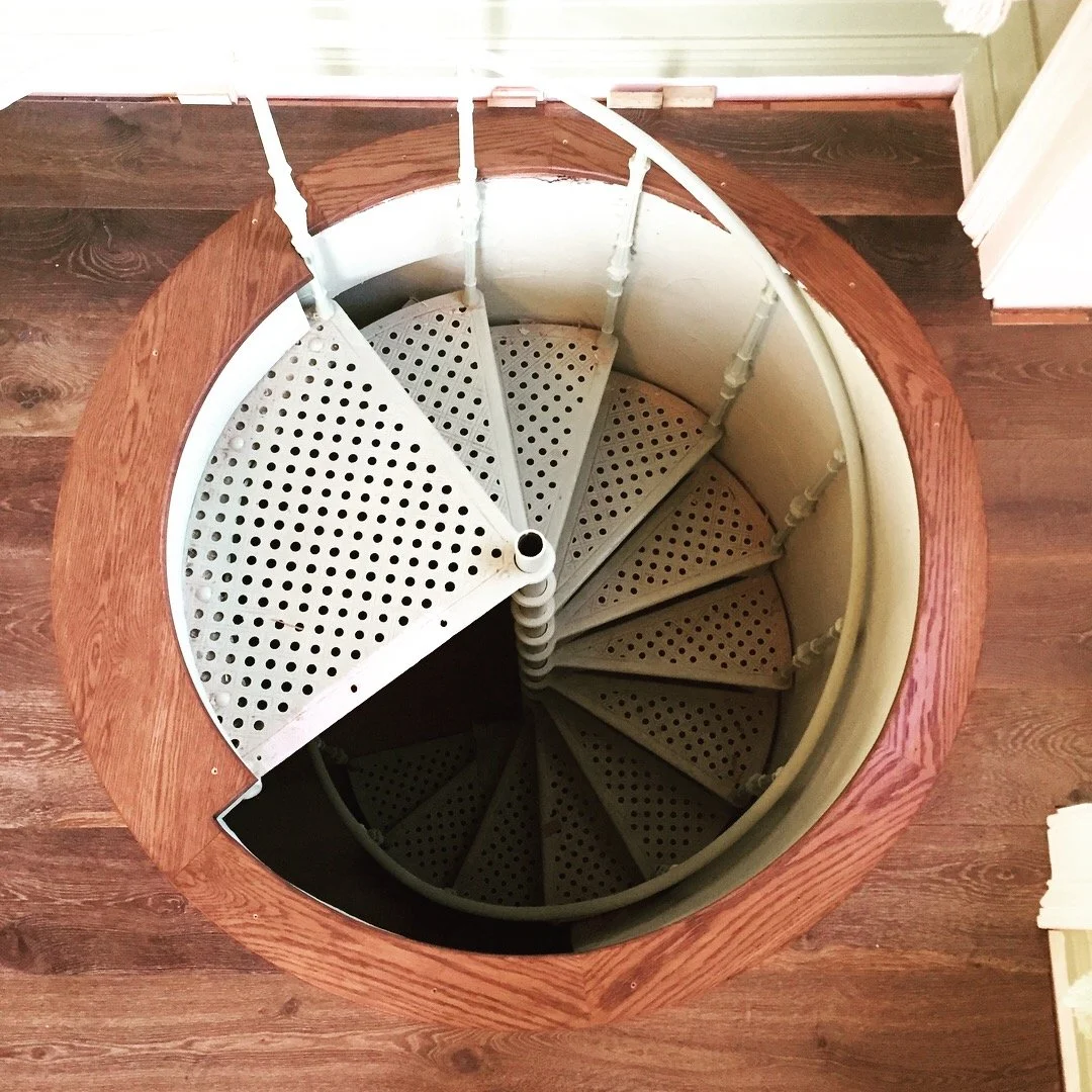 A spiral staircase with wooden handrails and perforated metal steps, viewed from above.