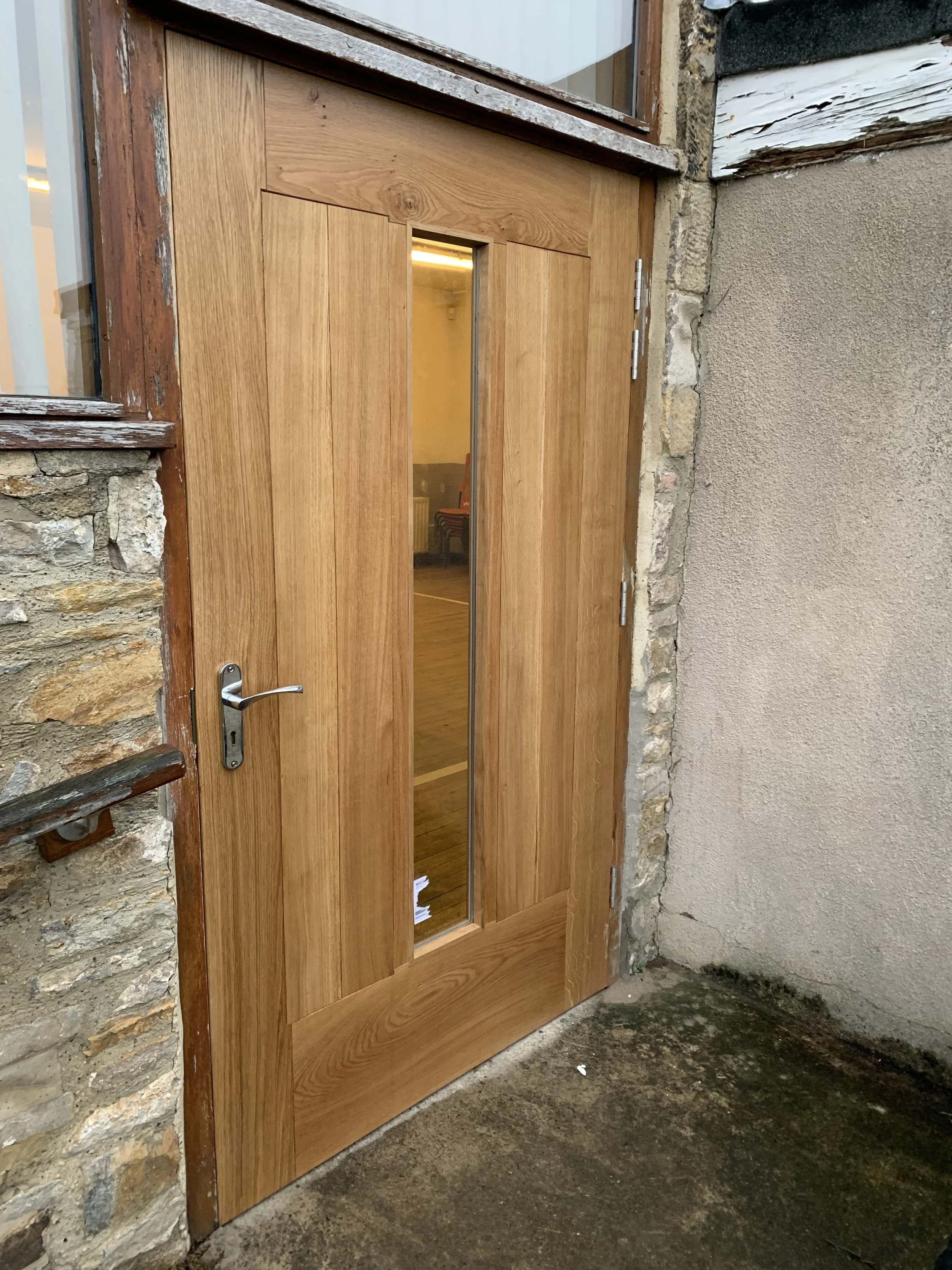 A wooden door with a glass panel in the center, set in a stone wall, with a metal handle on the left side.