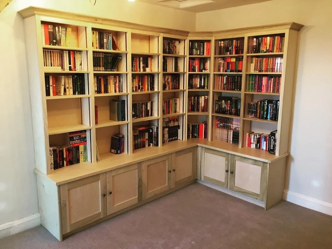 A corner wooden bookshelf filled with books in a living room, with closed cabinet doors at the bottom.