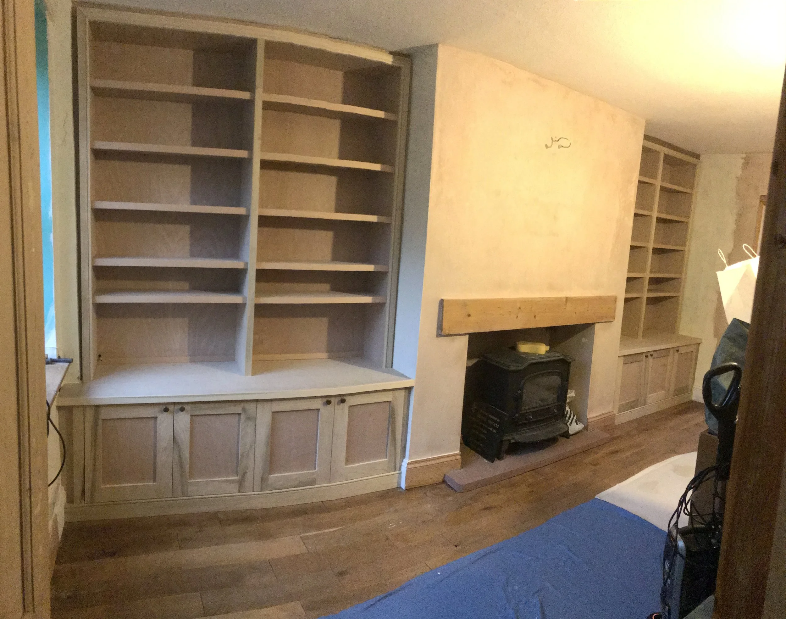 Empty wooden bookshelves in a room with a wooden floor and some household items.