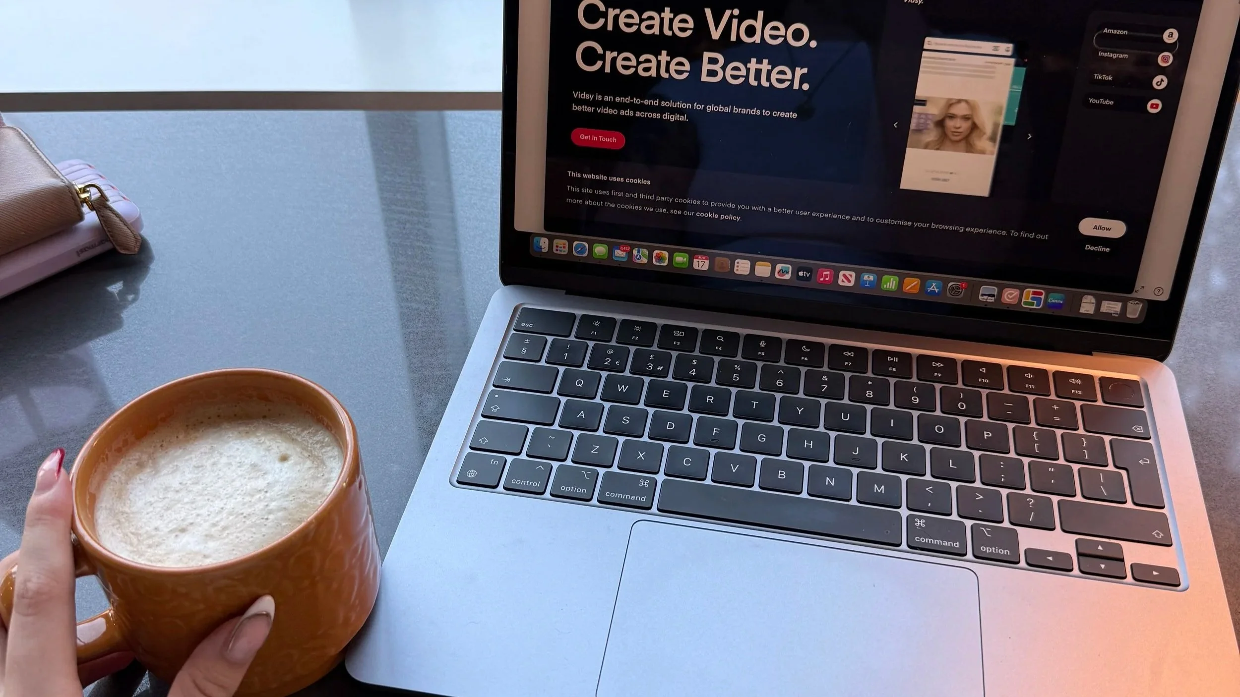 Laptop displaying a video advertising website beside a cup of coffee and pink handbag