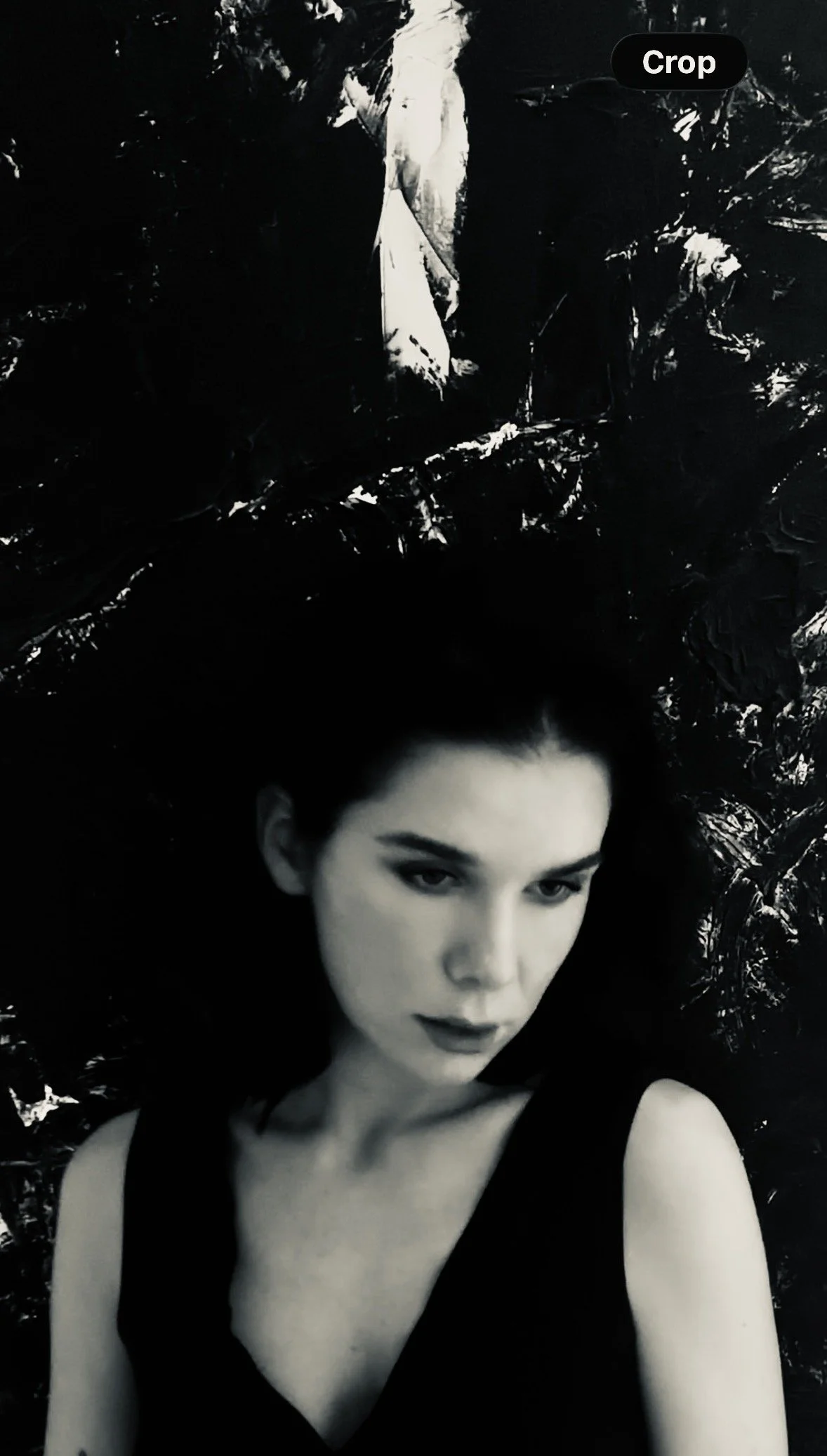 Black-and-white portrait of a woman with dark hair wearing a sleeveless black dress against a textured dark background