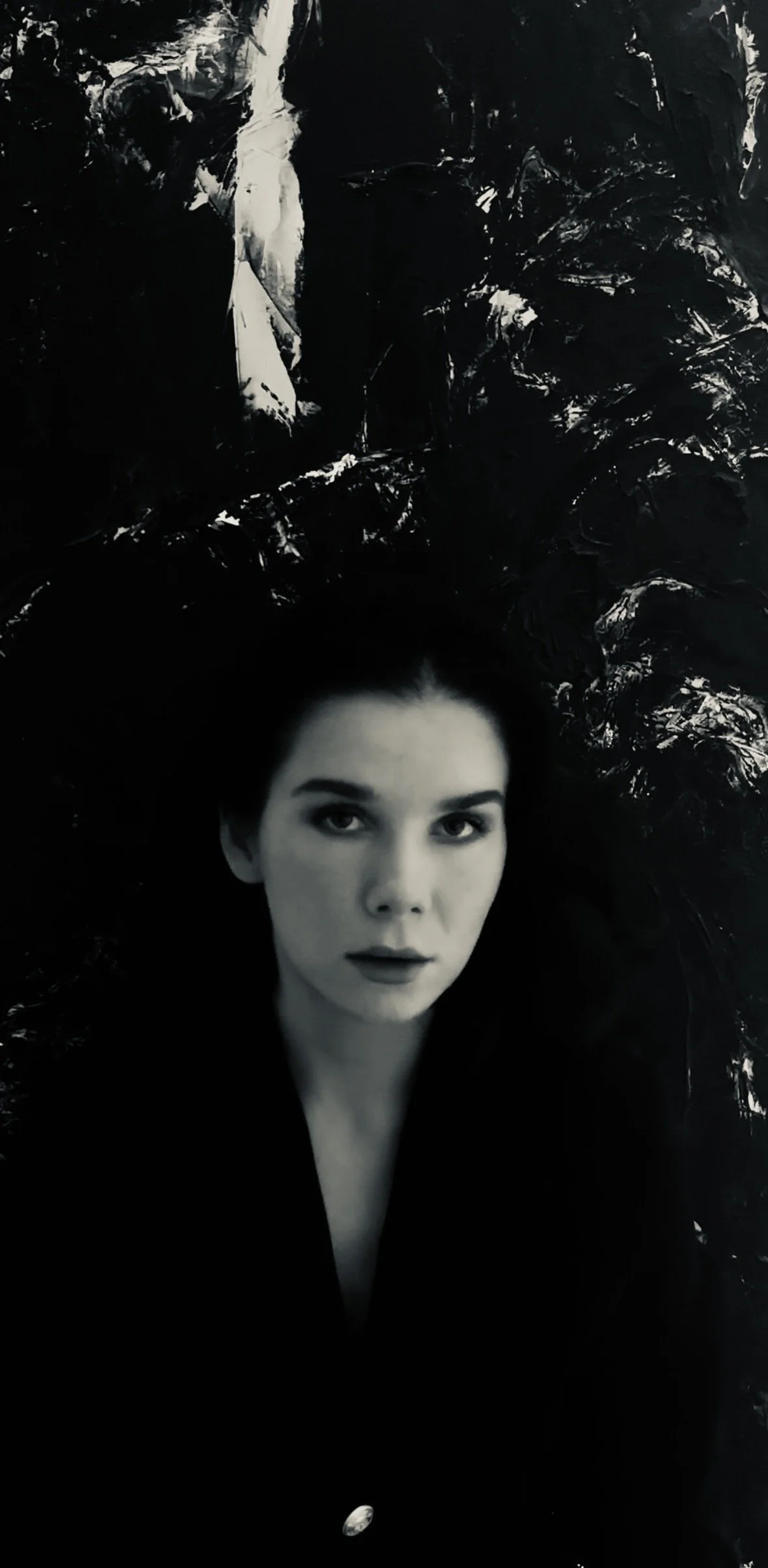 Black-and-white portrait of a woman with dark hair against a textured, shadowy background