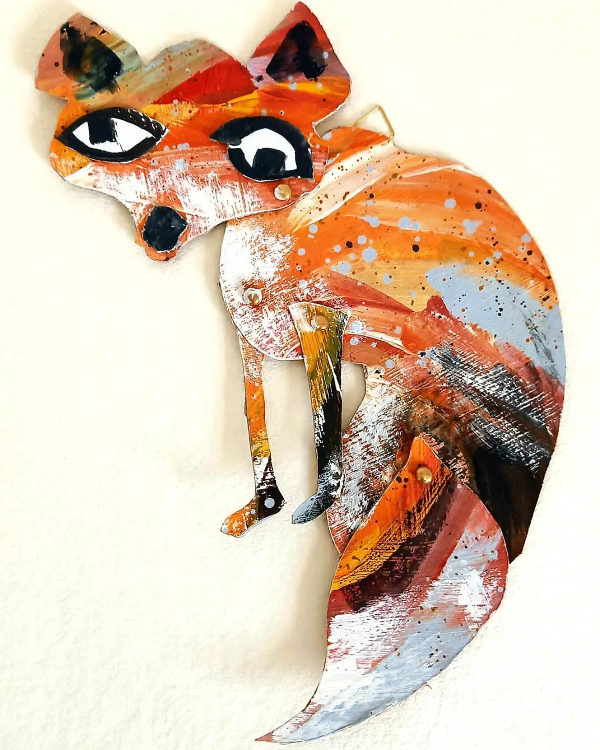 Colorful abstract fox sculpture with prominent black and white eyes, painted in shades of orange, red, black, with splashes of white and blue.