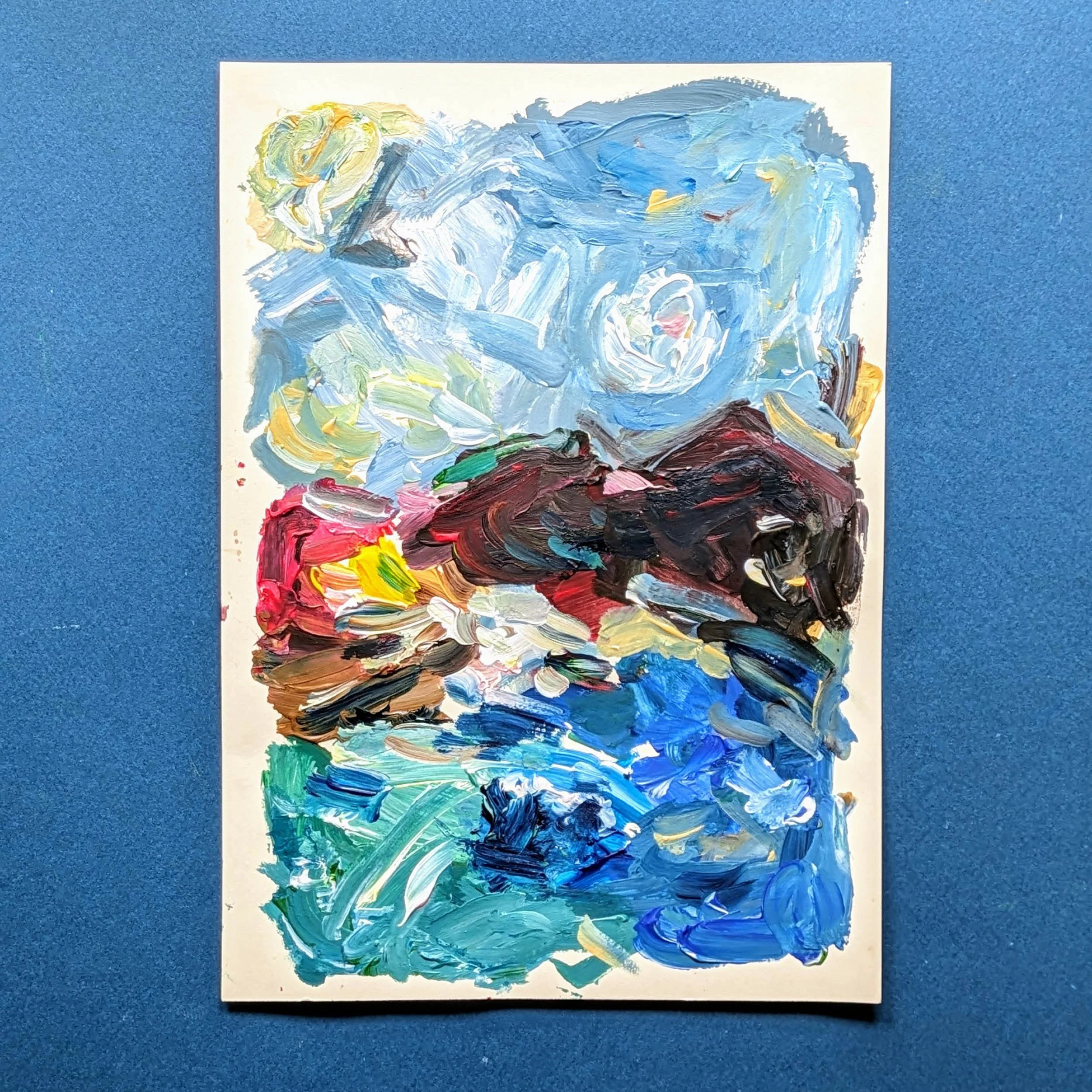 Abstract painting with thick, swirling strokes of blue, white, yellow, red, green, brown, and black paint on a white canvas, placed on a blue surface.