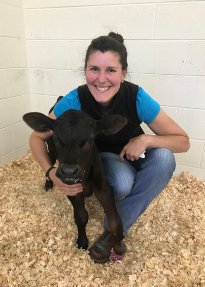 Smiling woman kneeling beside a black calf on wood shavings