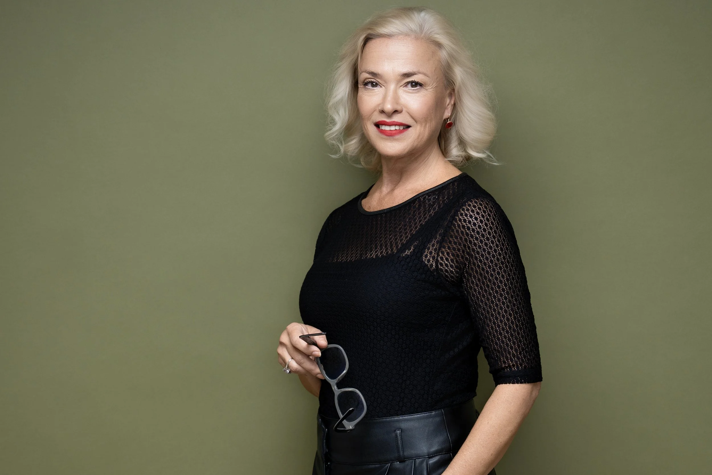 Professional studio headshot of a blonde woman against an olive-green background
