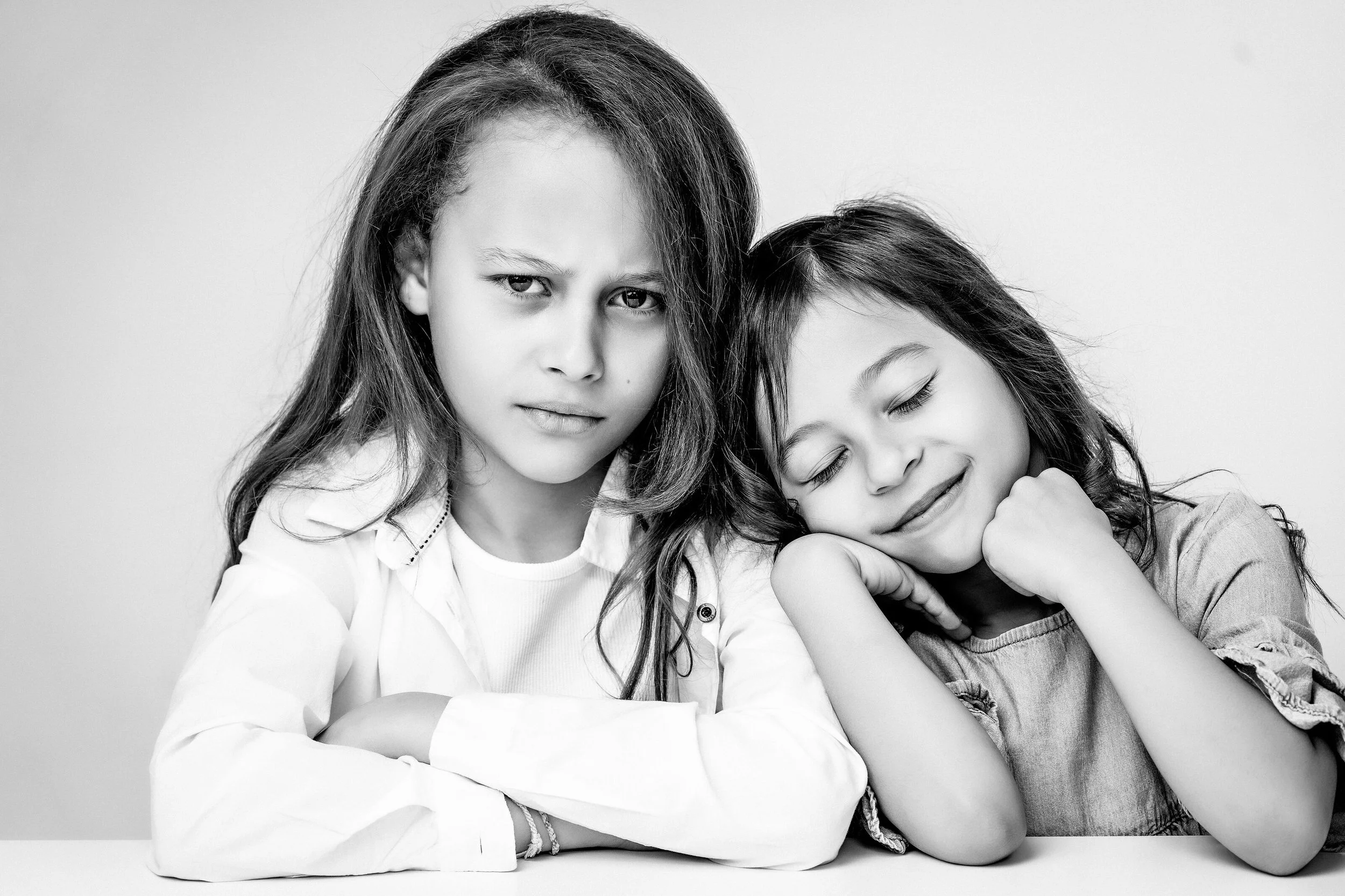 An elegant black-and-white portrait of two sisters, celebrating their individual personalities and special connection. Timeless sibling and children's studio photography by Lucas Gudaniec Photography in the Annecy and Geneva area.
