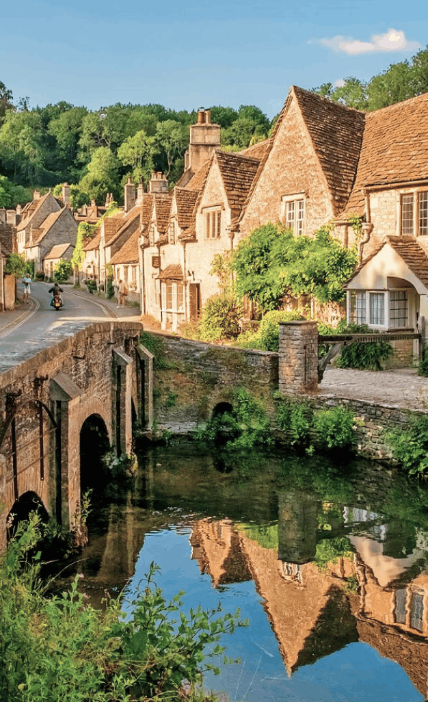 Cotswold village with honey-colored stone cottages, a stone bridge, and reflections in a calm stream