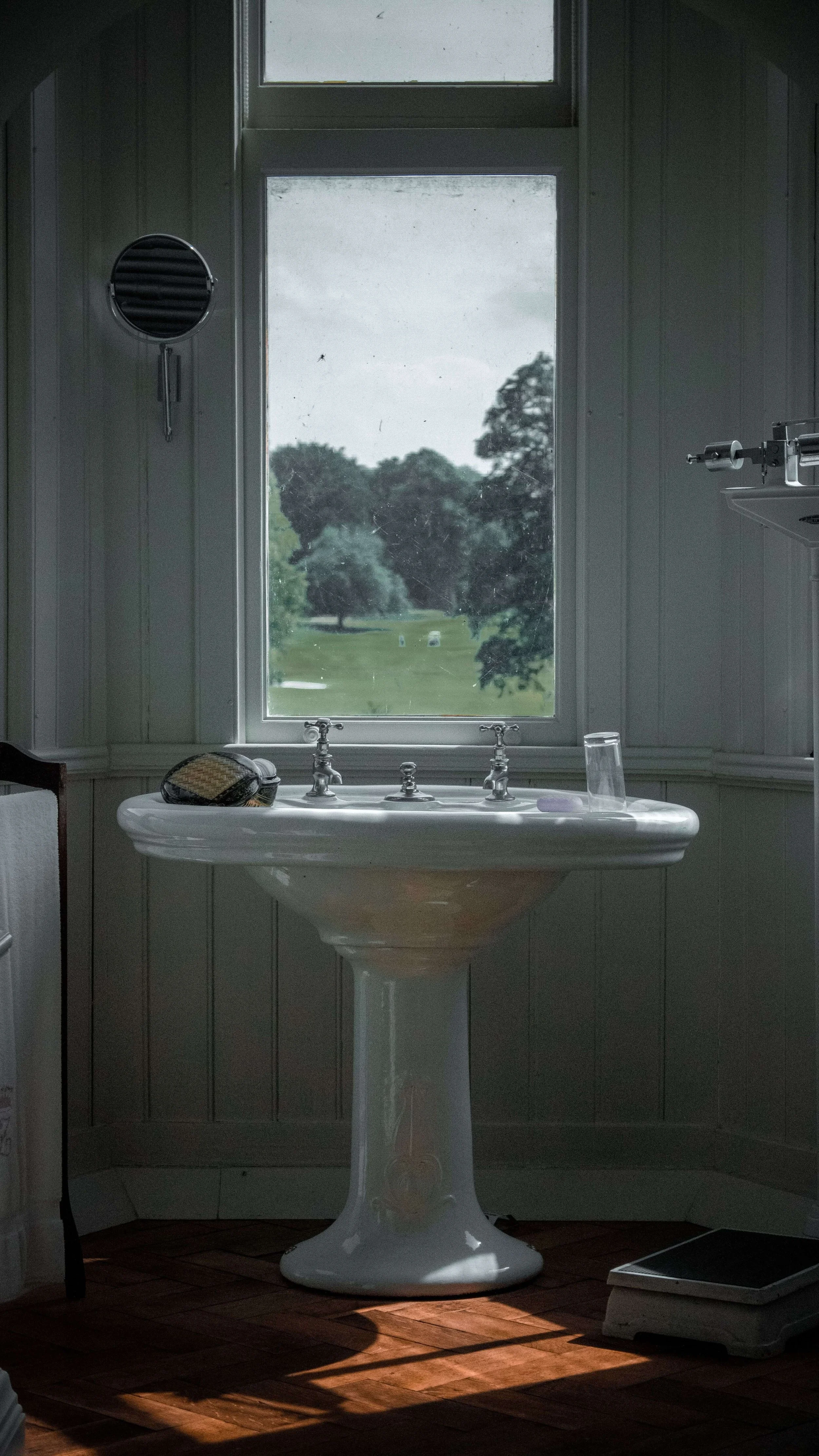 Vintage white pedestal bathroom sink beneath a window overlooking a green landscape