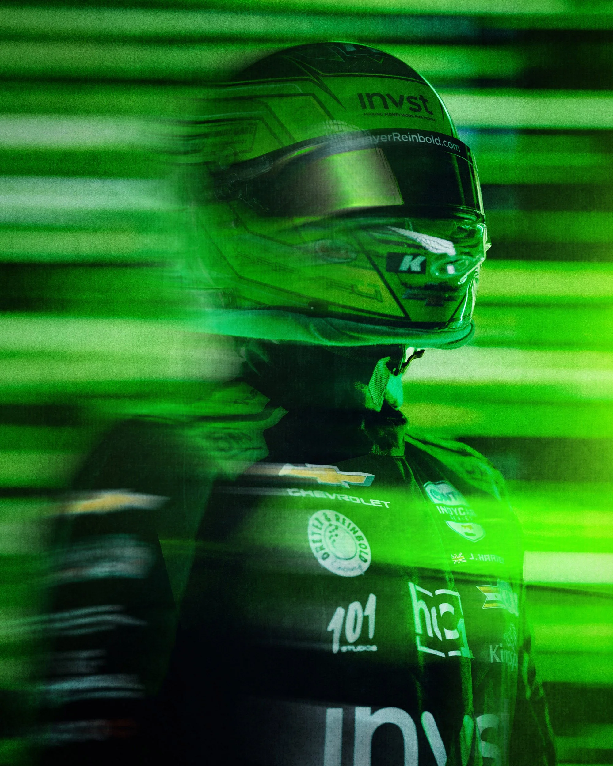 Green-tinted close-up of a NASCAR driver wearing a helmet and racing suit with sponsor logos. Jack Harvey for INVST