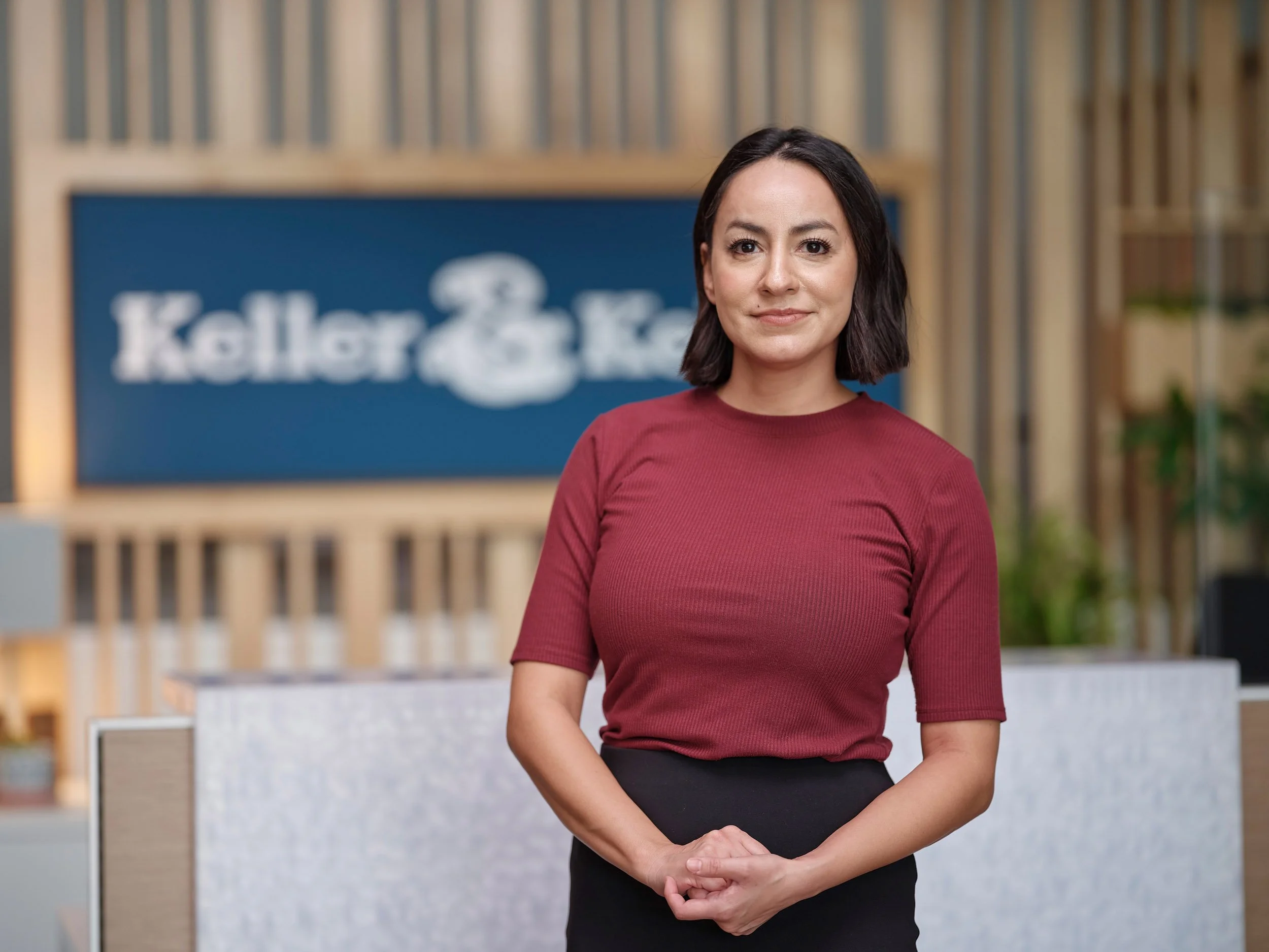 Woman in a burgundy shirt standing in front of a blurred Keller & Keller sign