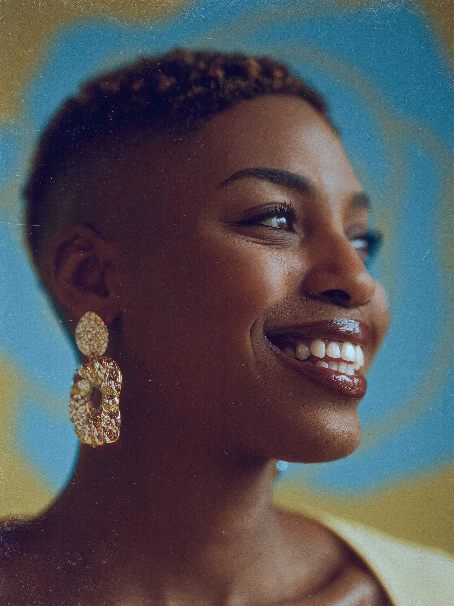 Close-up portrait of a smiling Black woman wearing large gold earrings against a blue background