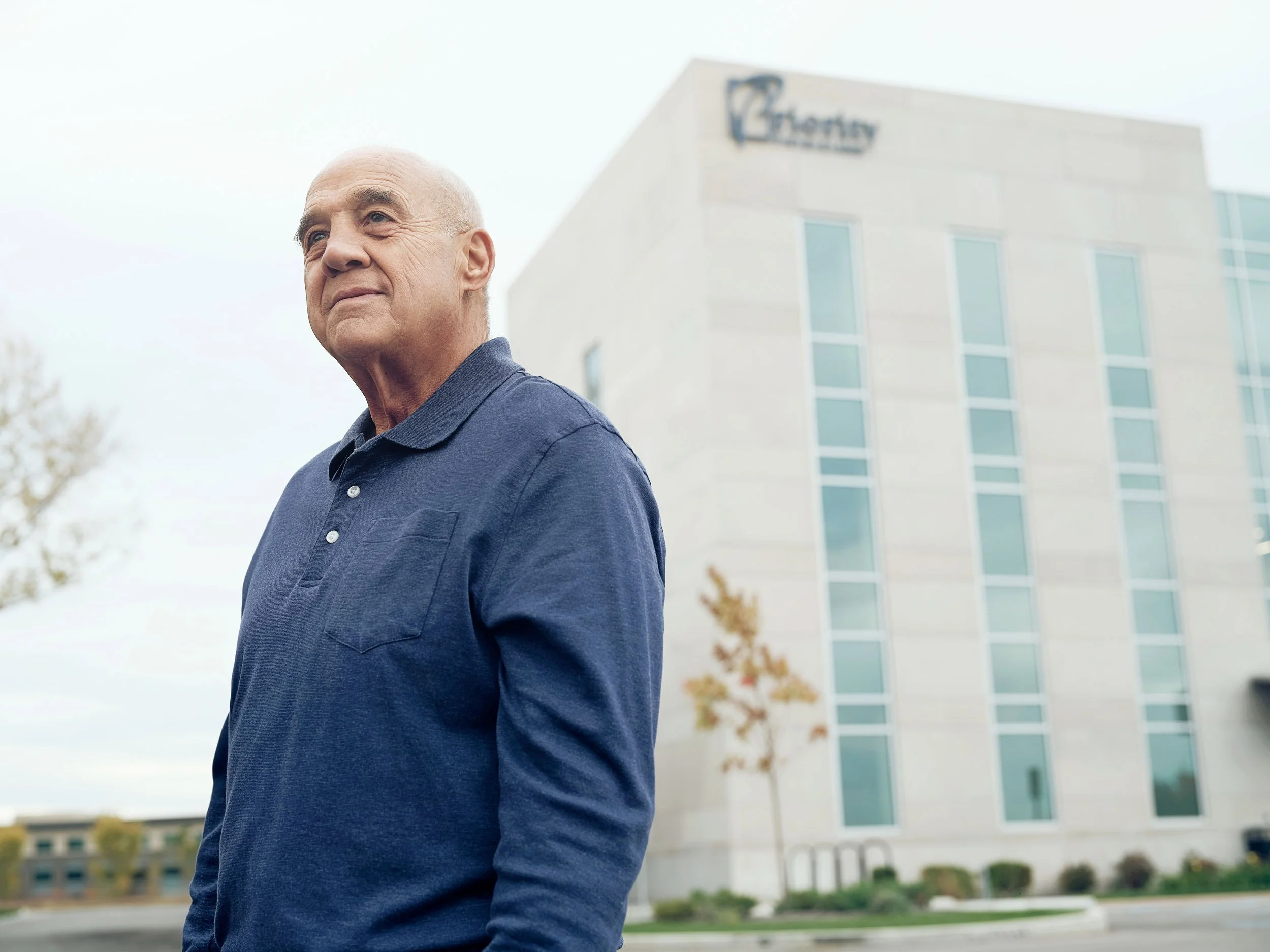 Older man in a blue polo shirt standing outside a senior living community building