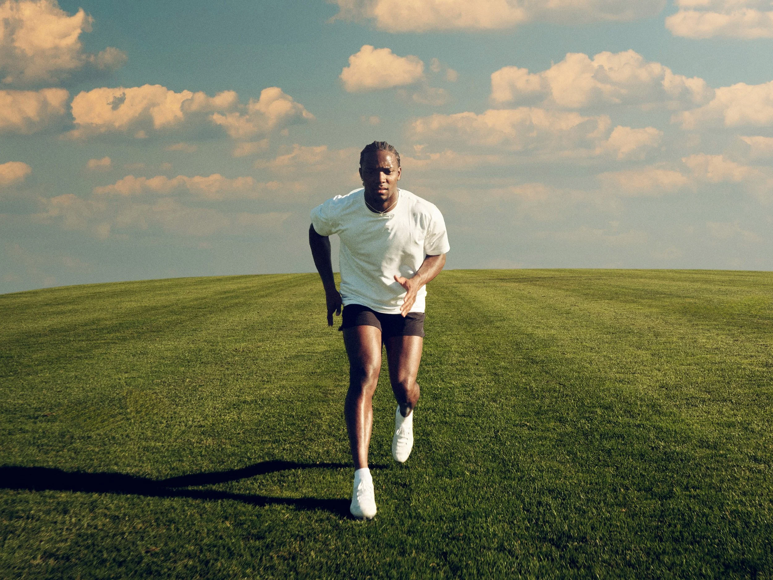 Man jogging across a grassy field beneath a cloudy blue sky