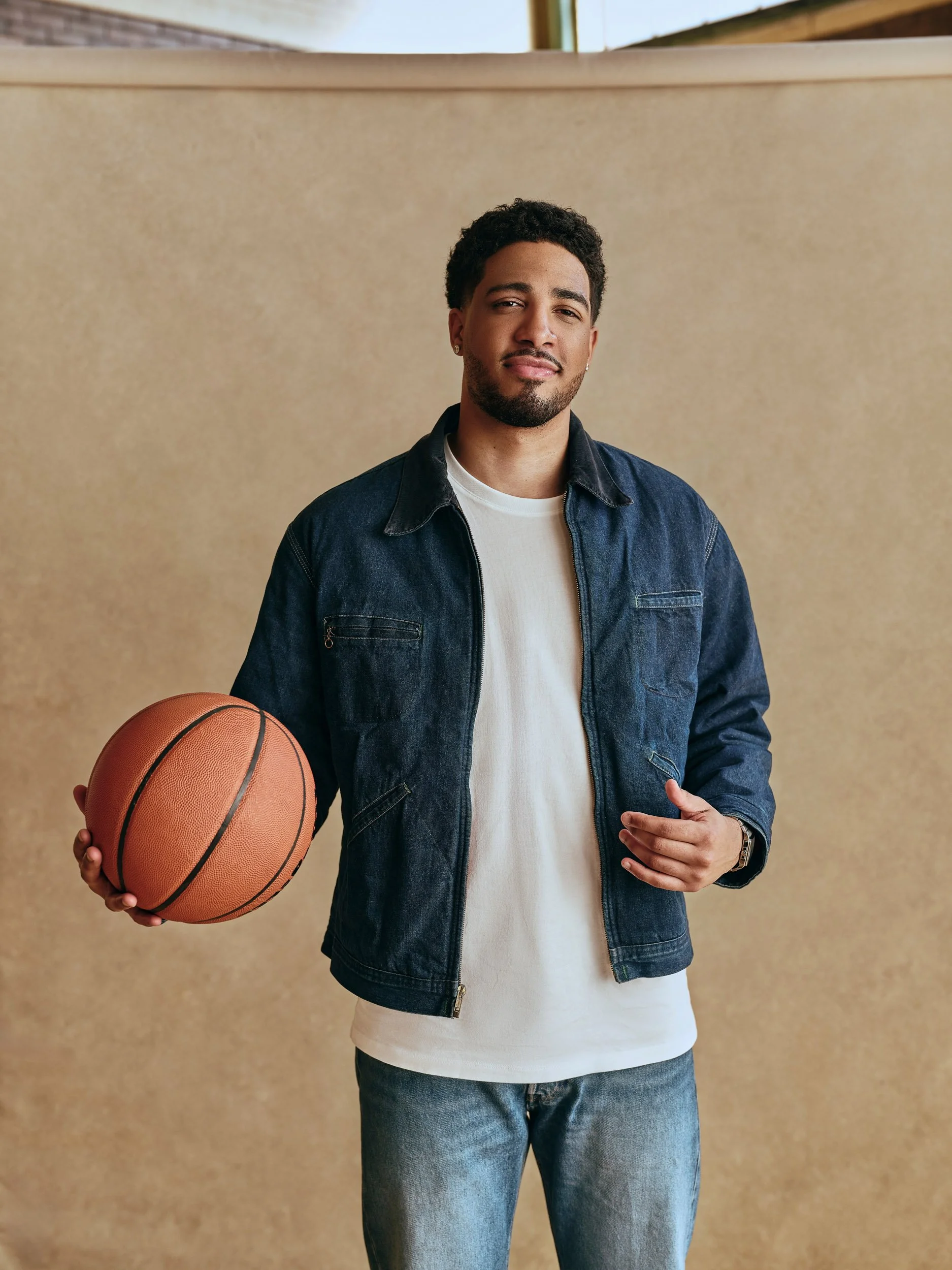 Tyrese Haliburton  holding a basketball while standing indoors against a beige wall.