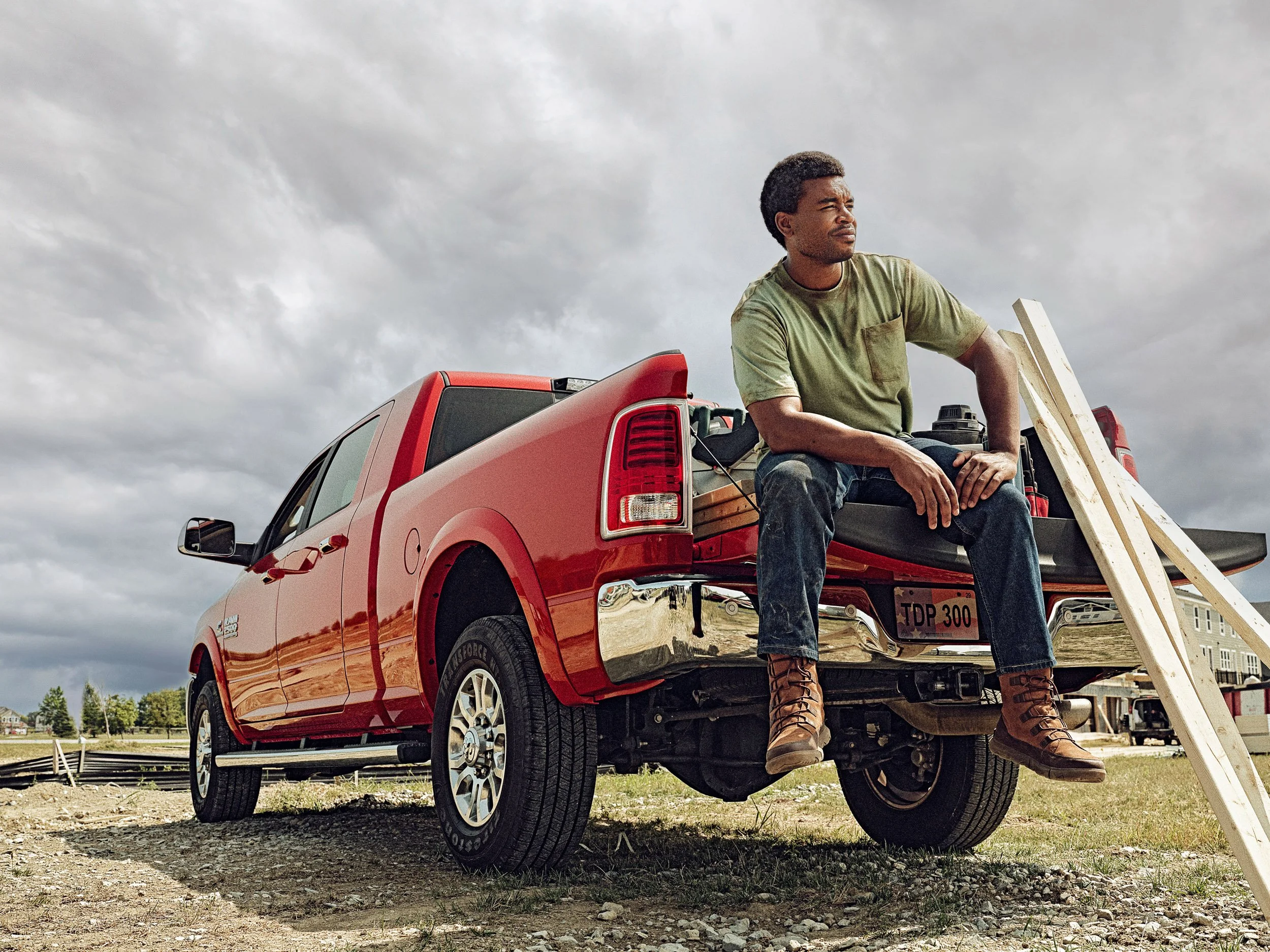 Construction worker sitting on a red pickup truck loaded with lumber at a building site