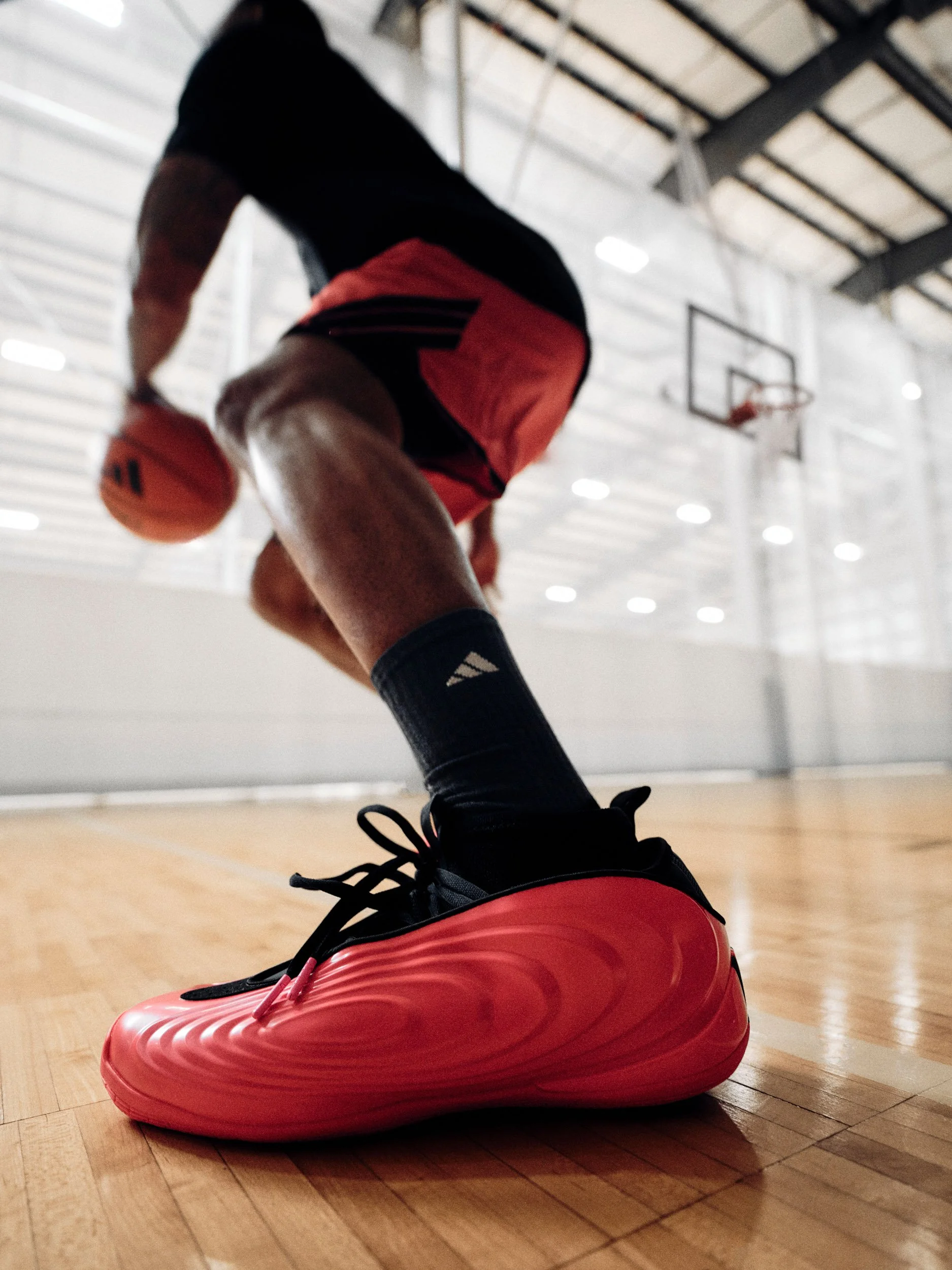 Close-up of a basketball player wearing red and black shoes on an indoor court