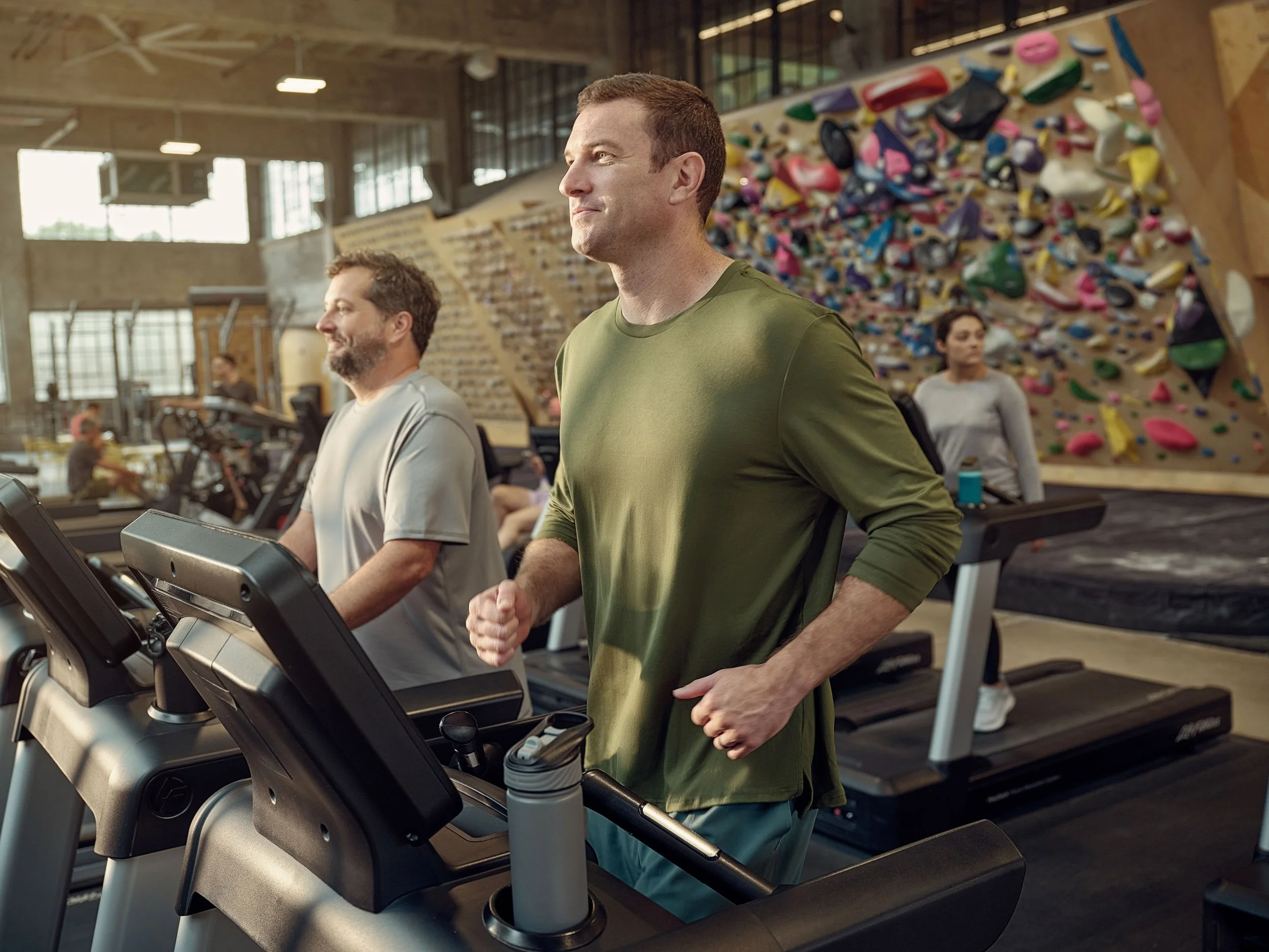 People exercising on treadmills in a modern gym with an indoor climbing wall
