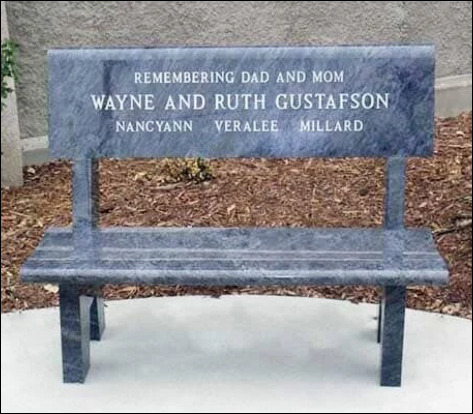 Blue granite memorial bench with engraved text honoring deceased family members, positioned outdoors on a concrete surface.