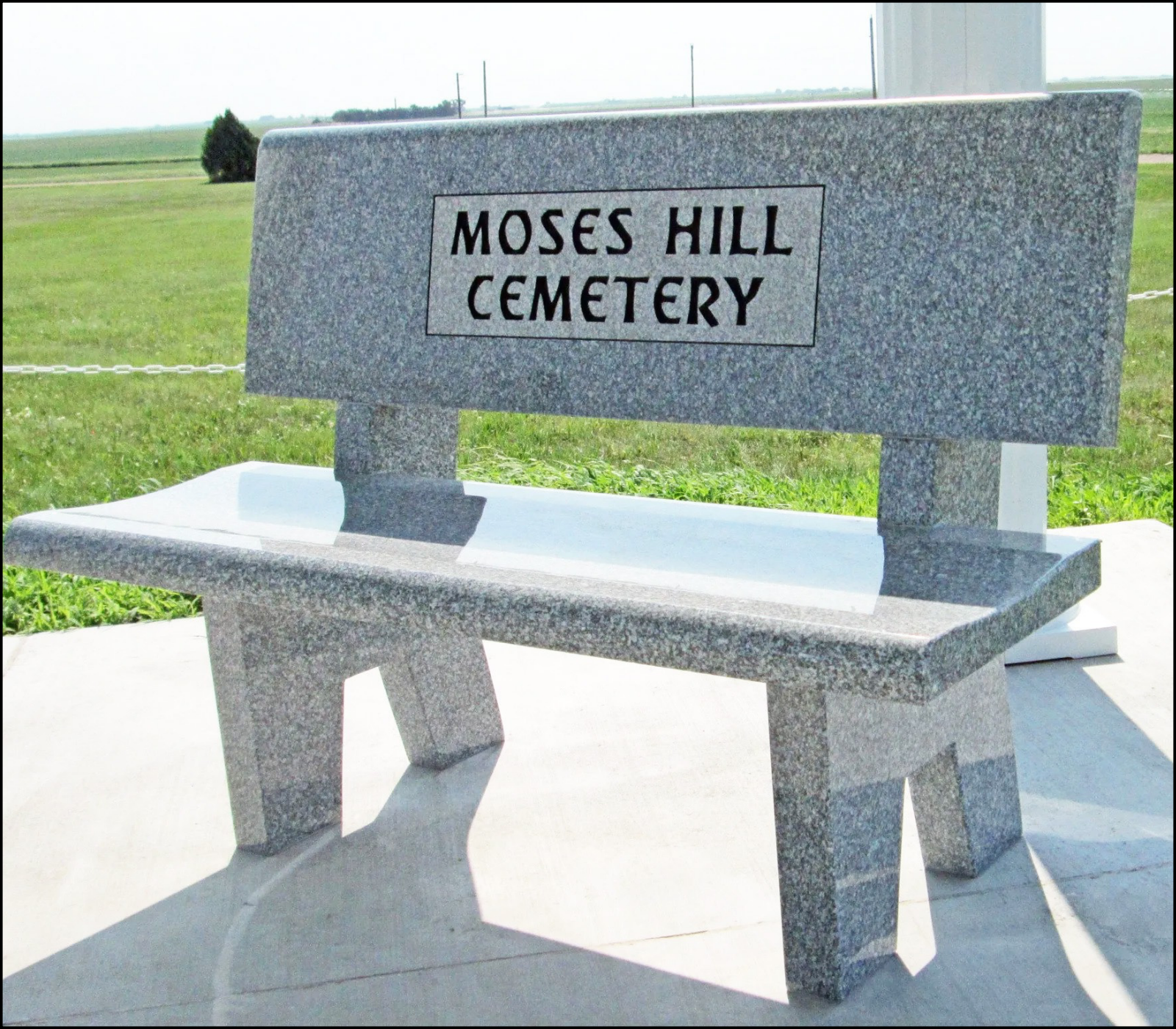 A granite bench with a sign reading 'Moses Hill Cemetery' in a grassy open field.