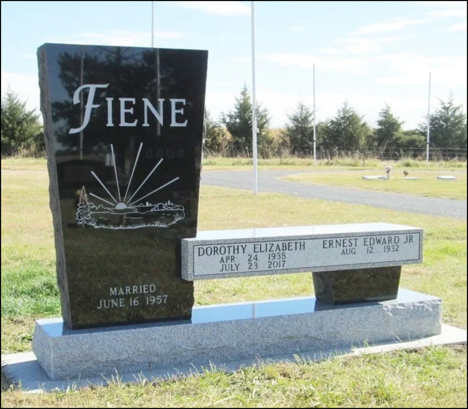 Gravestone for Dorothy Elizabeth and Ernest Edward Jr., with Dorothy's birth and death dates, and Ernest's birth date, located in a grassy area with trees and flagpoles in the background.