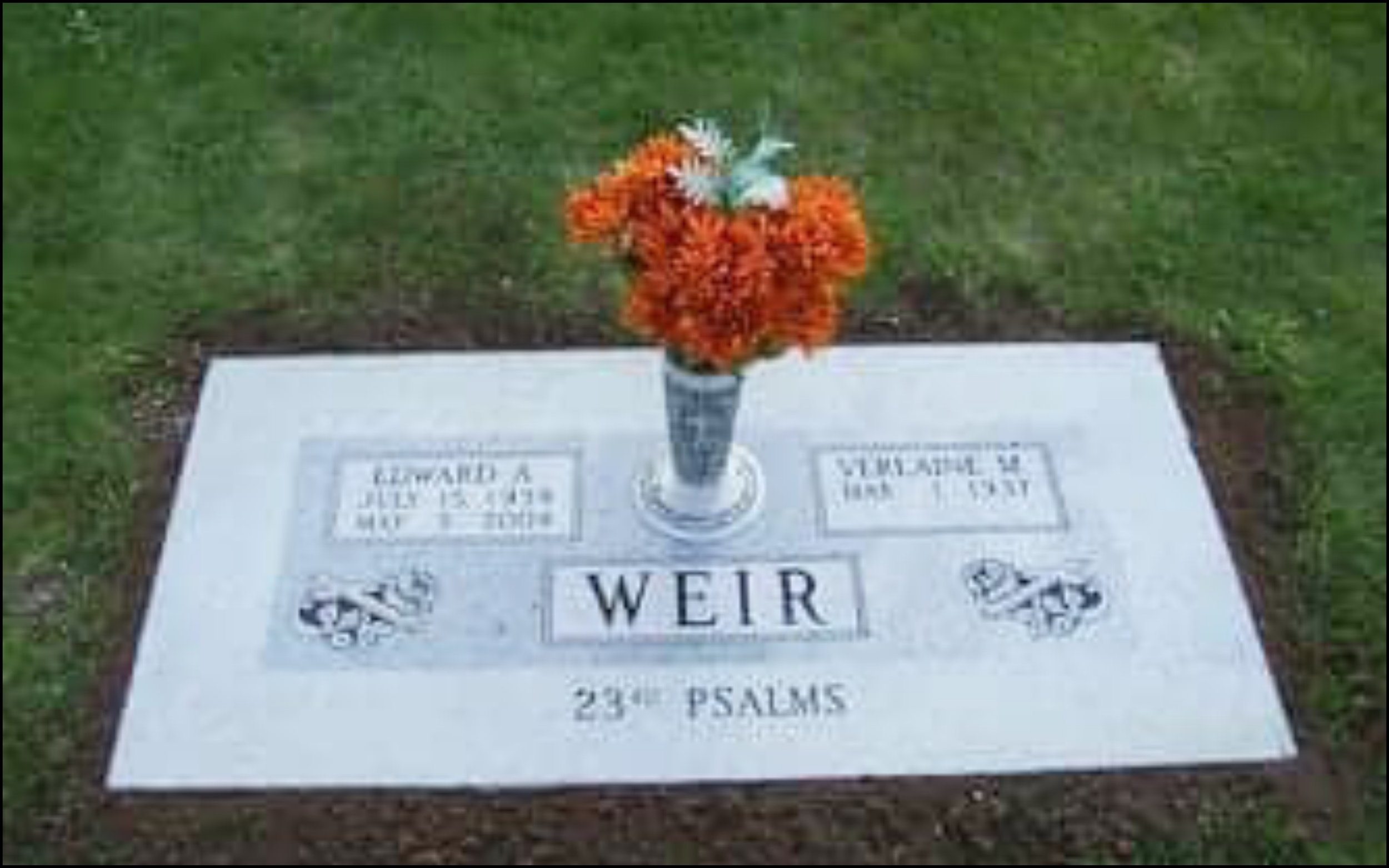 Gravestone with a bouquet of orange and white flowers placed on top, with the name WEIR inscribed on the stone.