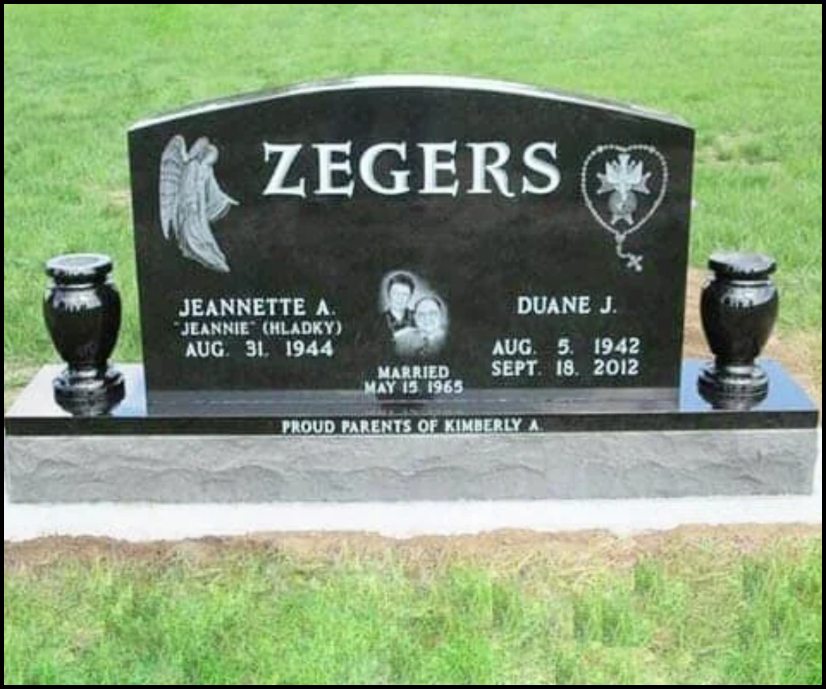 A black granite headstone for the Zegers family, with engraved angels and memorial details for Jeannette A. and Duane J., and a photo of the couple, set on a grassy area.