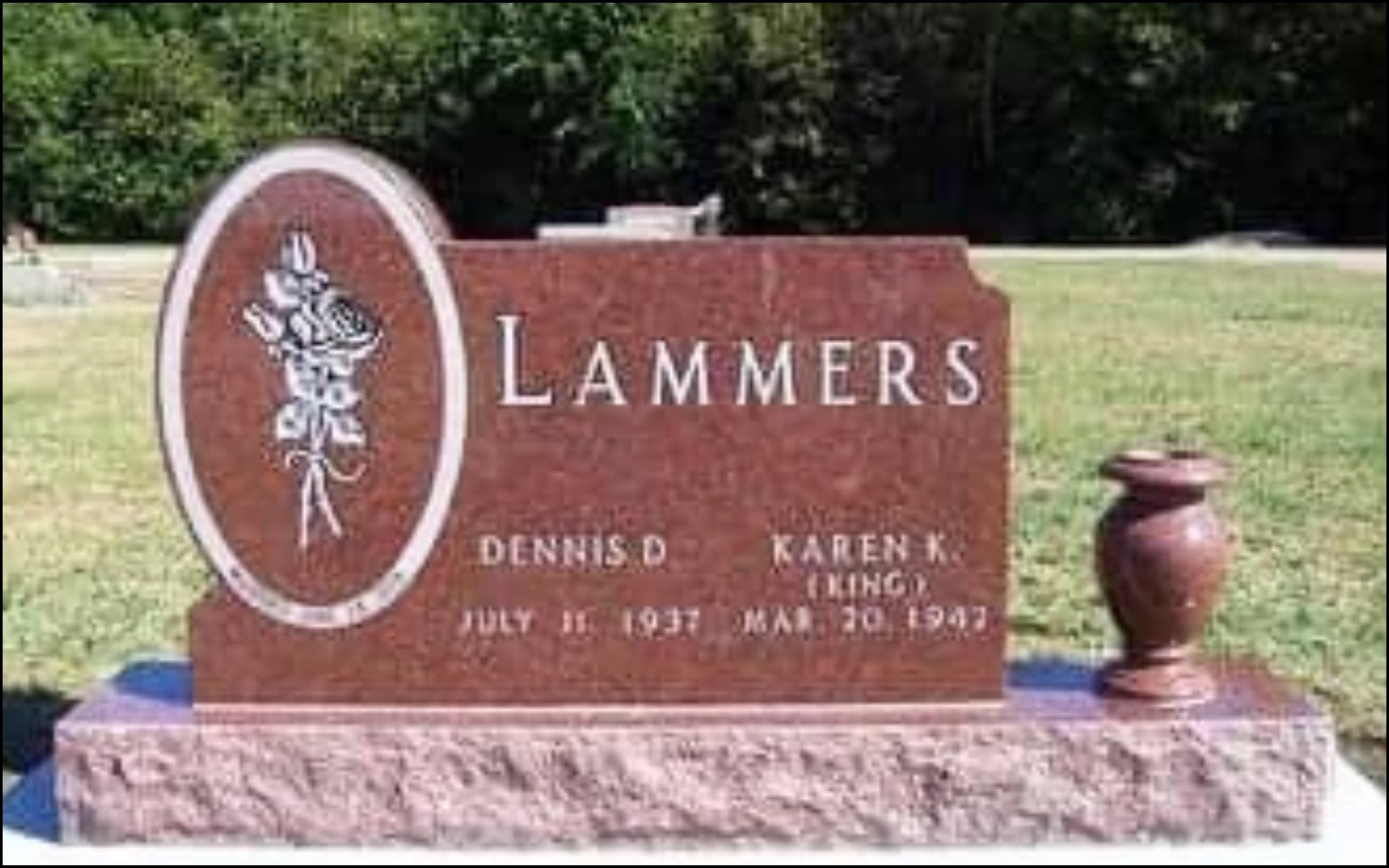 Red granite headstone for the Lammers family, featuring a carved torch and scroll design, with inscriptions of names and dates in a cemetery surrounded by grass and trees.